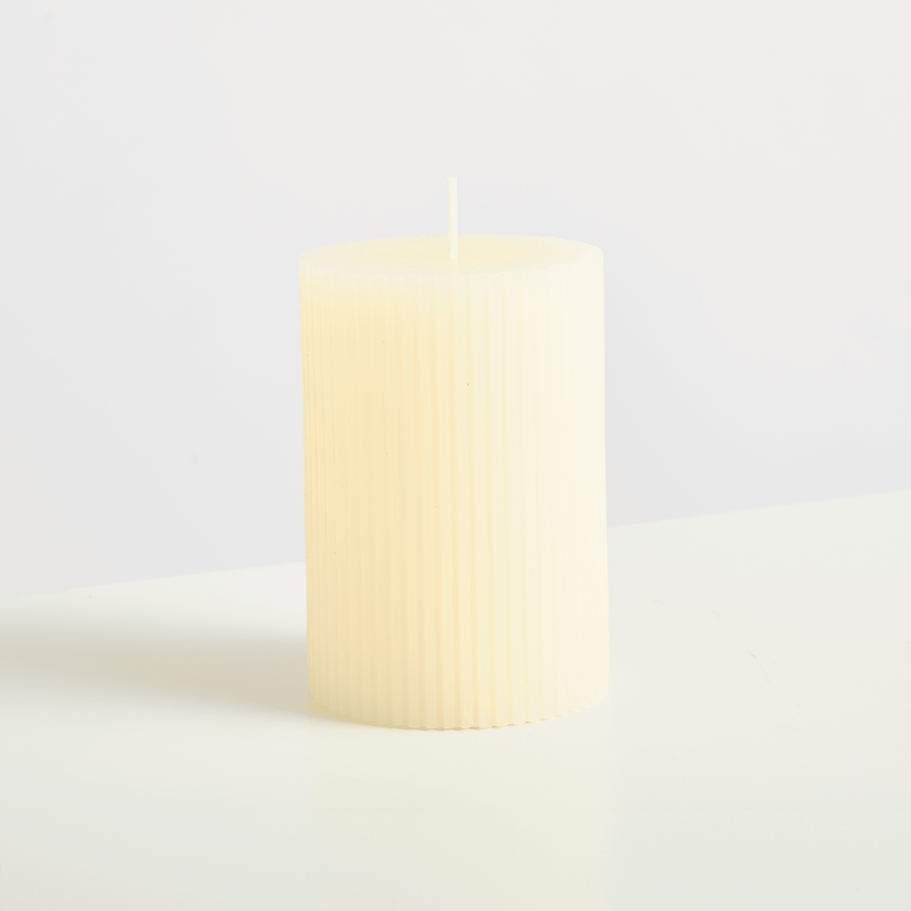 Eine einfache, zylindrische Kerze mit einer weichen, cremigen Farbe steht allein auf einer schlichten, hellen Oberfläche.