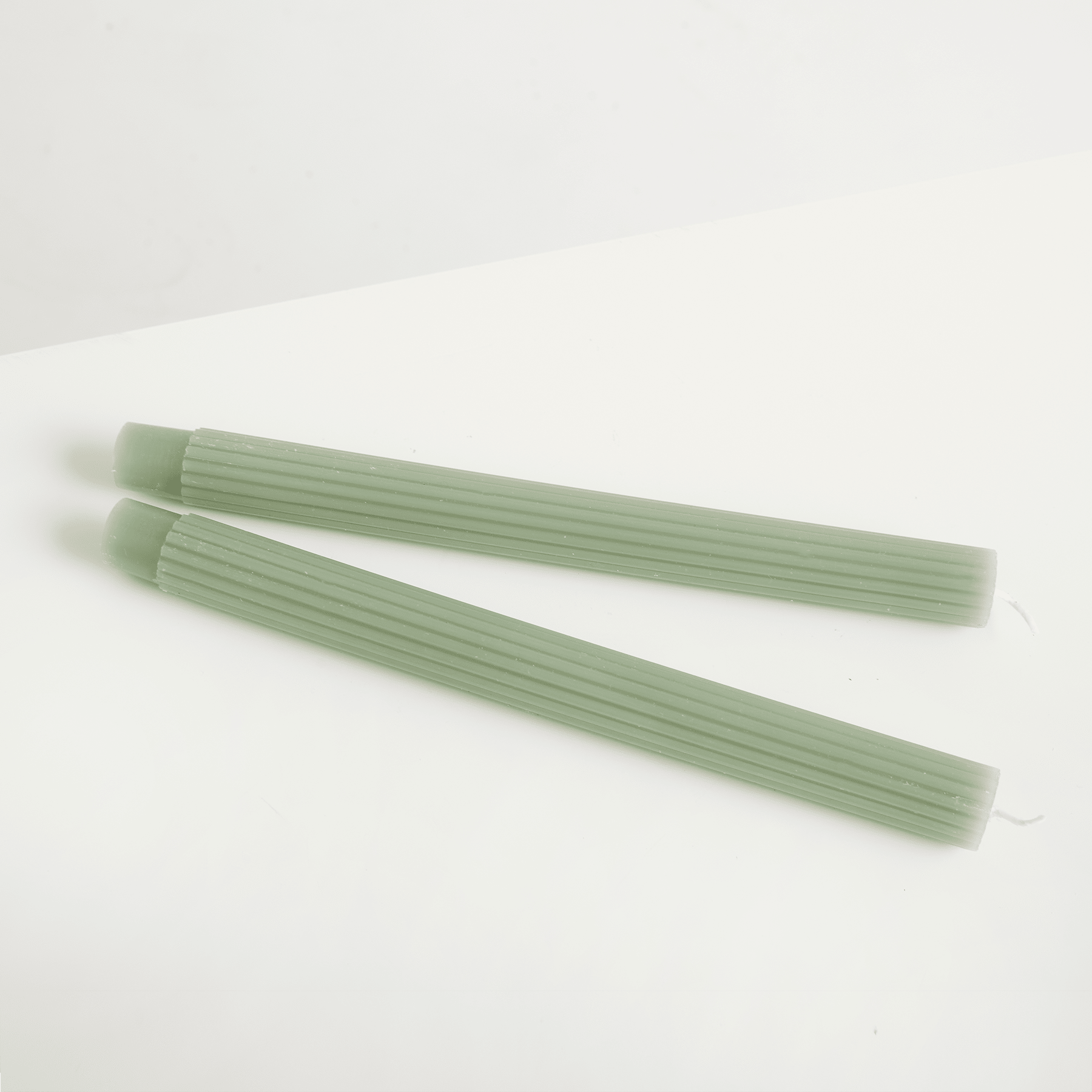 Zwei grüne Plastikstrohhalme liegen auf einem schlichten weißen Hintergrund.