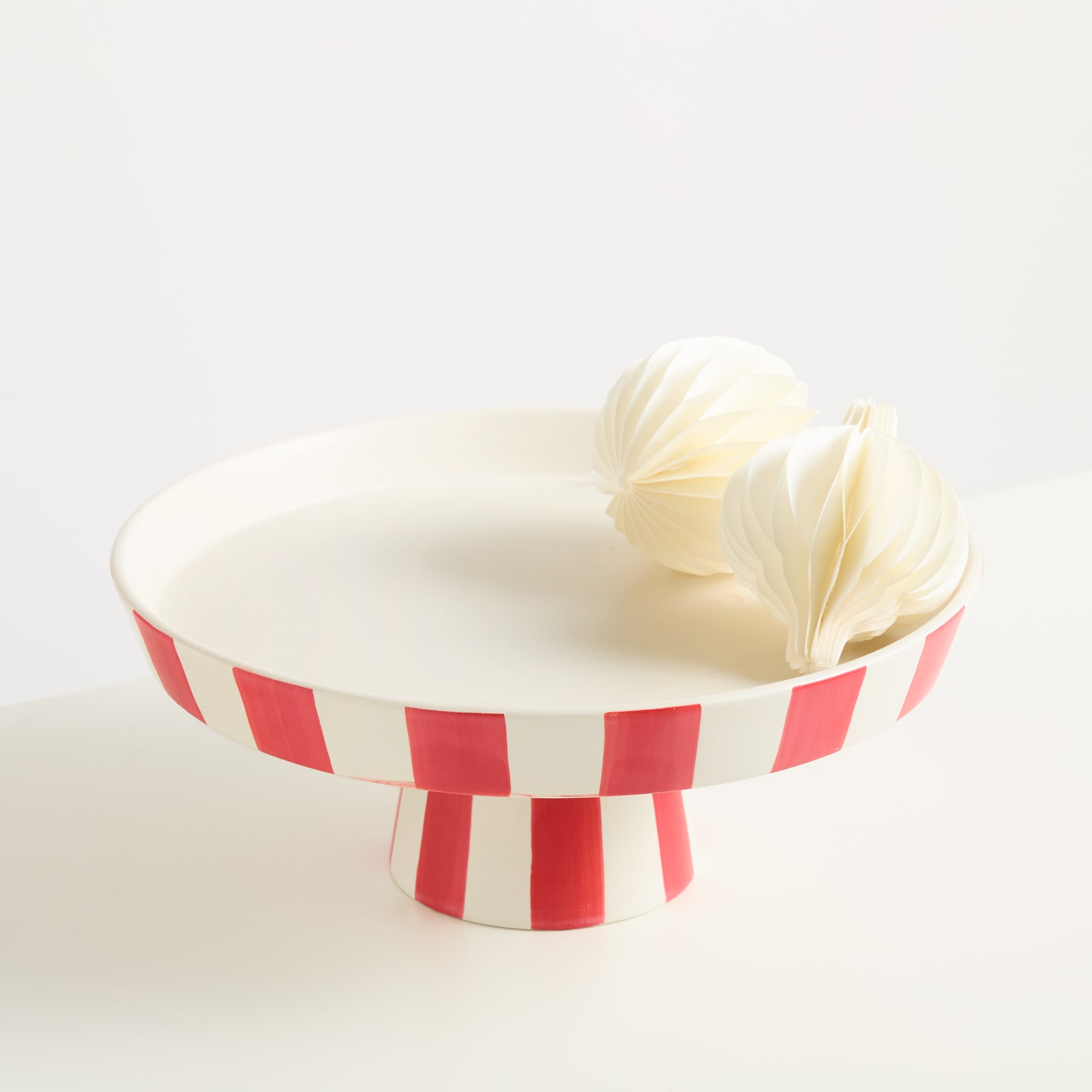 Ein rot-weiß gestreifter Tortenständer hält eine große, luftige weiße Baiser- oder Marshmallow-ähnliche Süßigkeit auf einem schlichten weißen Hintergrund.