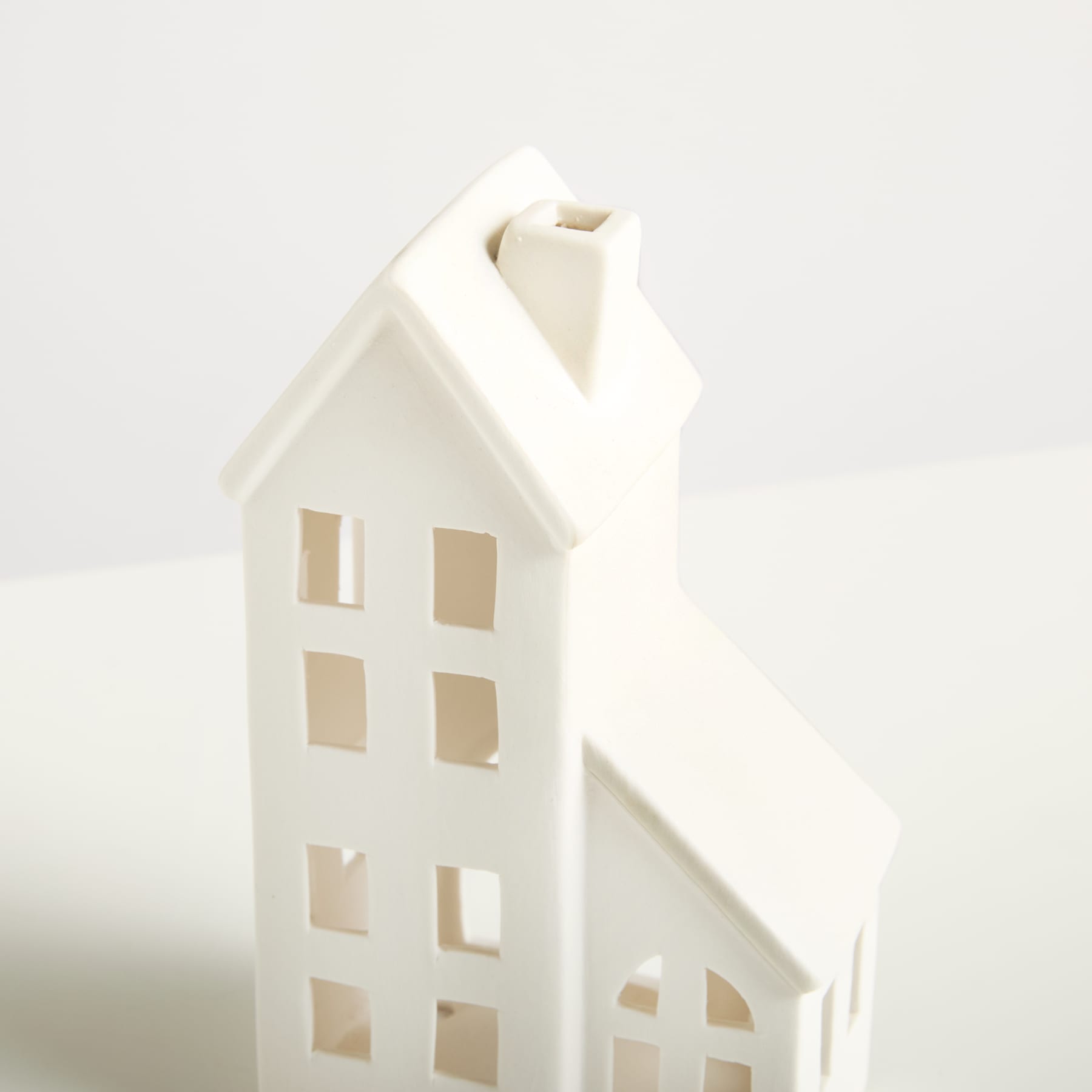 Ein einfaches, weißes Ornament oder eine Dekoration aus Keramik in Form eines Hauses steht vor einem schlichten, hellen Hintergrund.