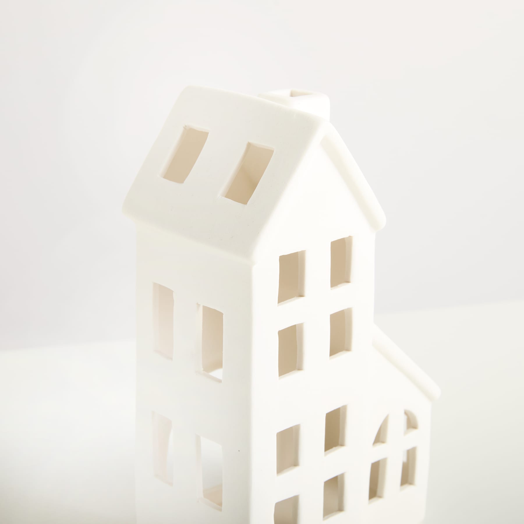 Ein einfaches, minimalistisches weißes Objekt in Form eines Hauses steht vor einem schlichten weißen Hintergrund und schafft eine klare und ruhige visuelle Komposition.