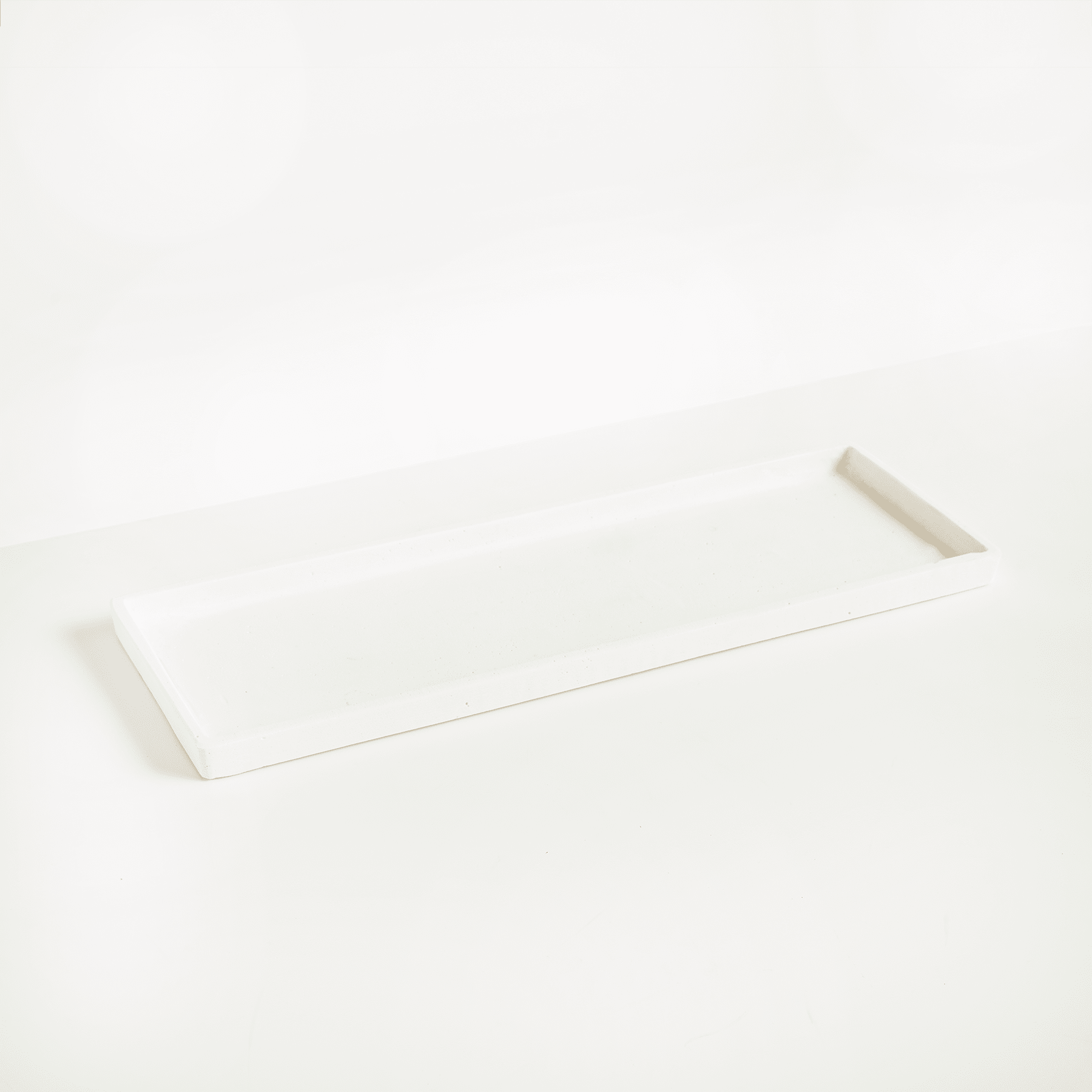 Ein einfaches, minimalistisches weißes rechteckiges Objekt, möglicherweise ein Regal oder Tablett, ruht auf einem schlichten weißen Hintergrund.