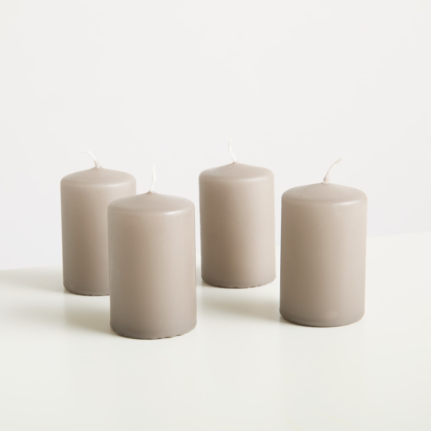 Vier weiße zylindrische Kerzen auf einem schlichten weißen Hintergrund angeordnet.