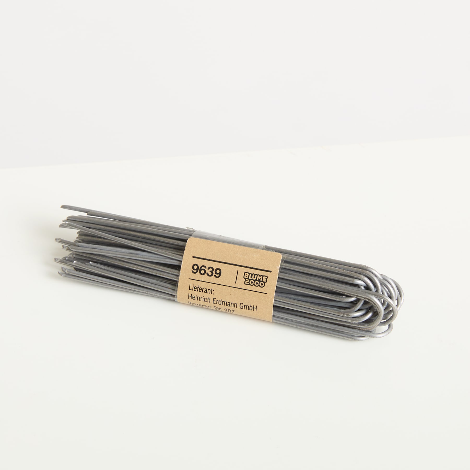 Auf einem schlichten weißen Hintergrund hängt ein Bündel grauer Metalldrähte, an dem ein Etikett mit dem Produktcode angebracht ist.