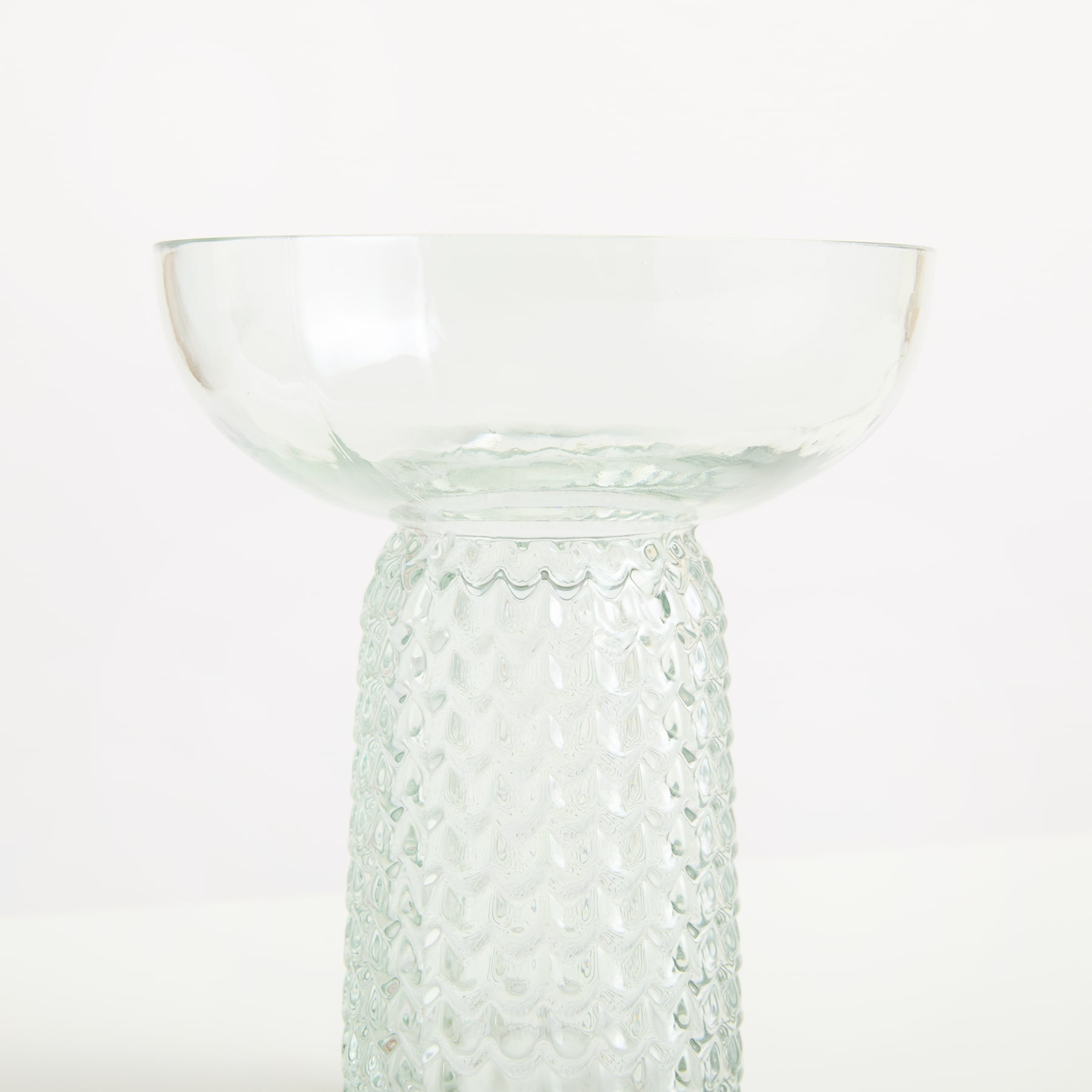 Eine klare Glasschale mit strukturiertem, gemustertem Stiel steht vor einem schlichten weißen Hintergrund.