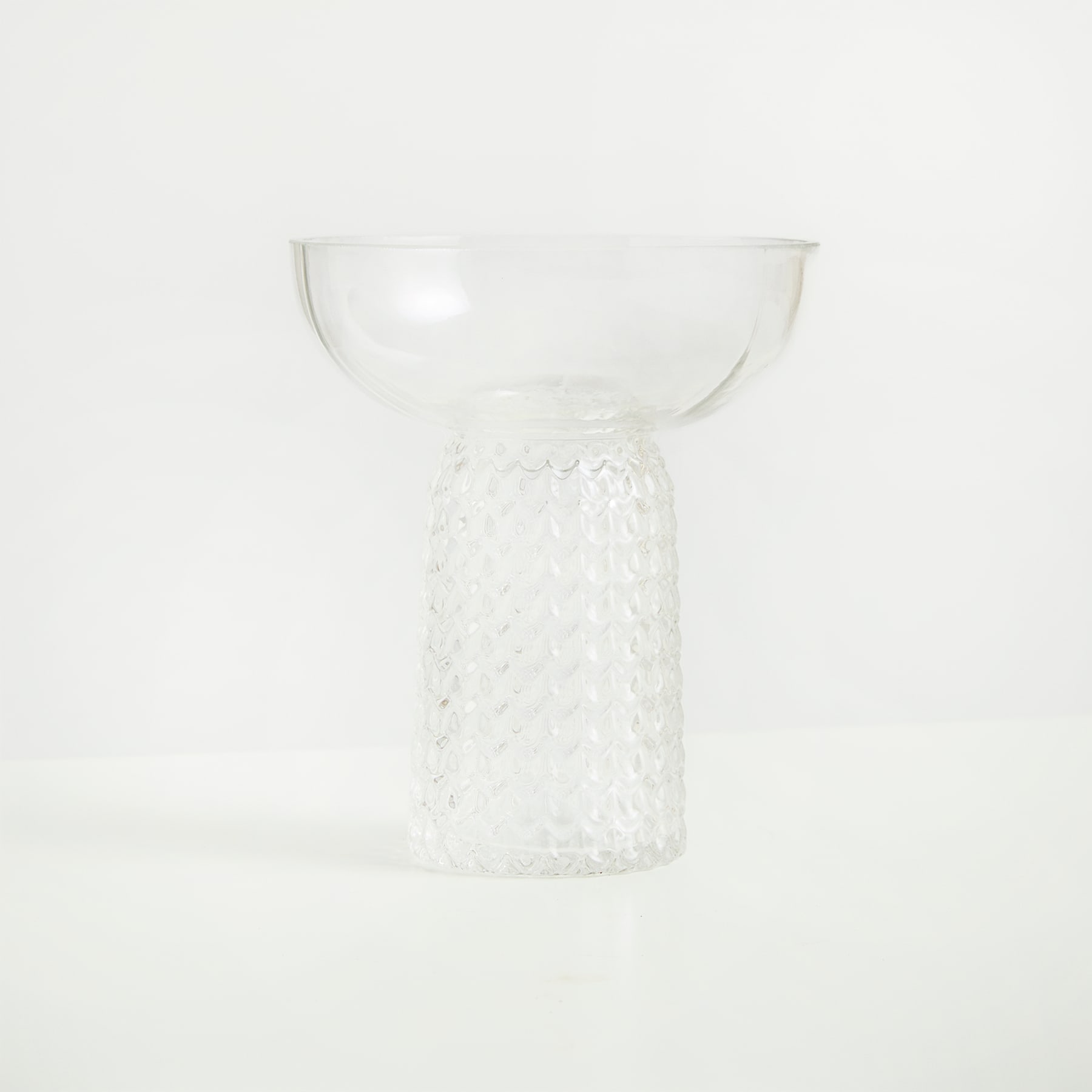 Auf einem schlichten weißen Hintergrund steht ein schalenförmiges Objekt aus klarem Glas mit strukturierter, gemusterter Außenseite.