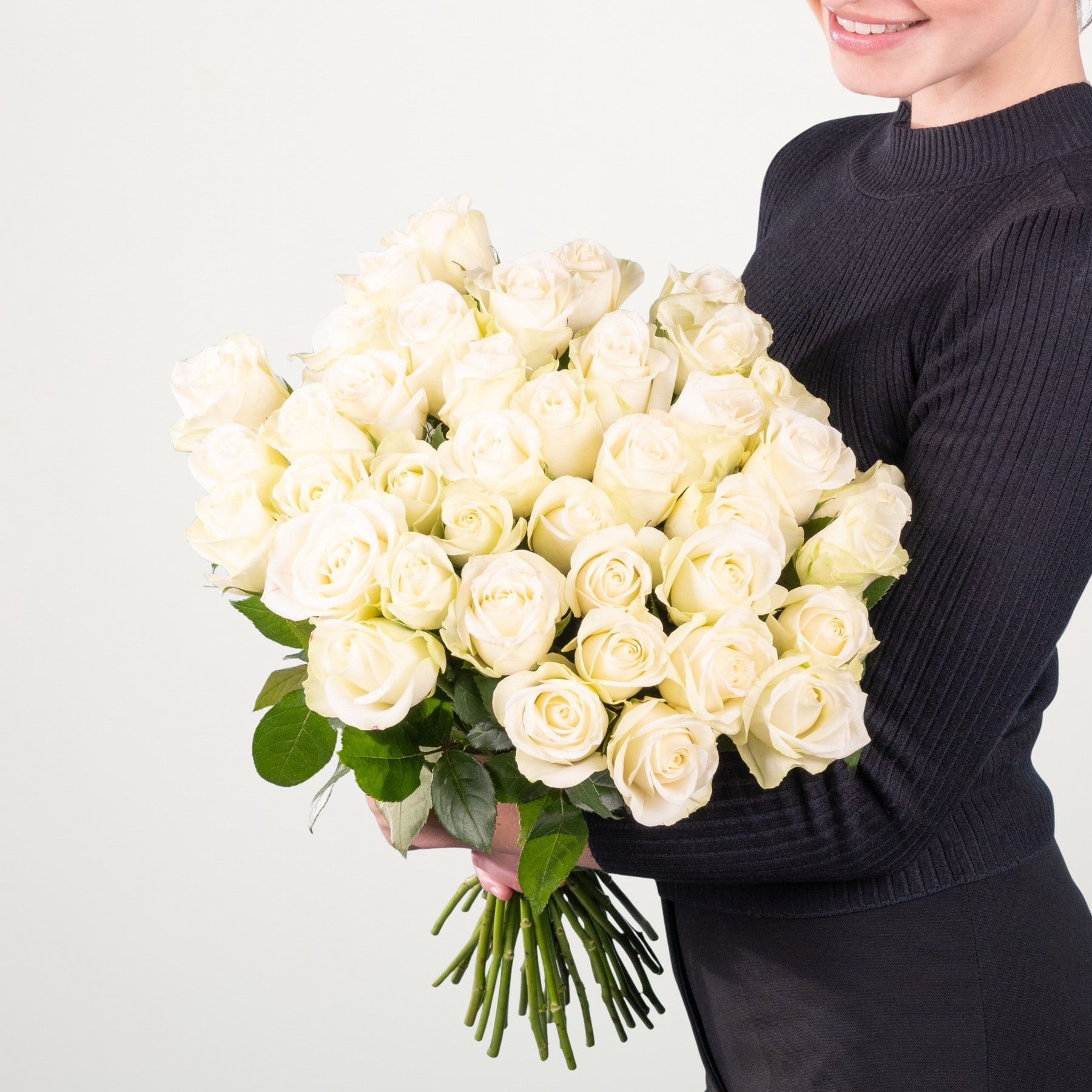 Eine Person in einem schwarzen Pullover hält einen großen Strauß wunderschöner weißer Rosen vor einem schlichten weißen Hintergrund.