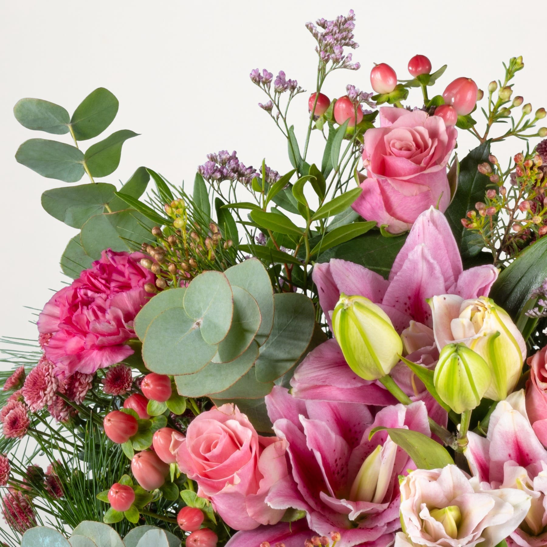 Ein farbenfroher Strauß verschiedener rosa und roter Blumen, darunter Rosen, Nelken und Tulpen, arrangiert mit üppigem Grün vor einem schlichten weißen Hintergrund.