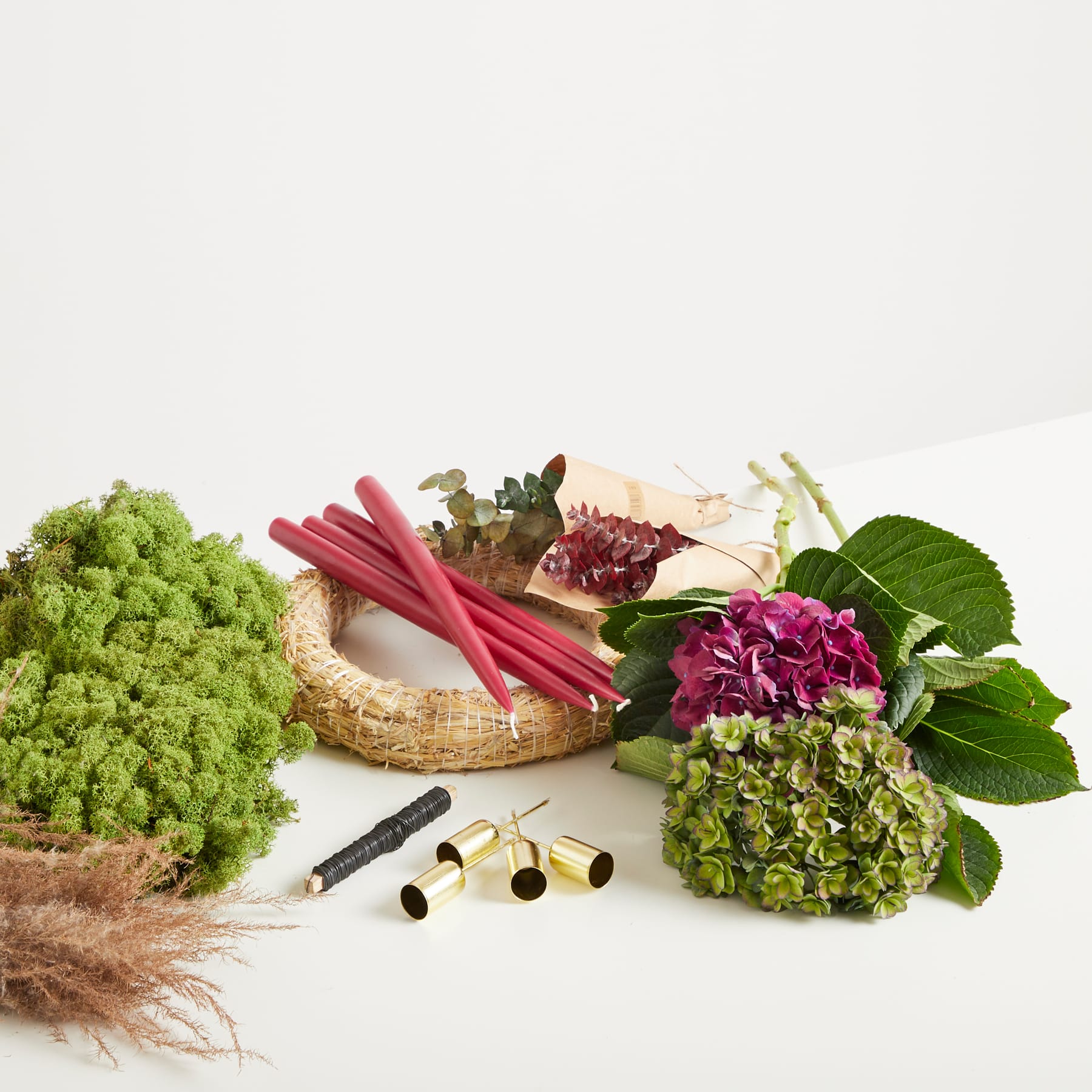 Ein farbenfrohes Arrangement aus frischen Produkten, darunter grünes Blattgemüse, rote Stiele und eine violette Blume, liegt auf einer Holzoberfläche vor einem schlichten weißen Hintergrund.