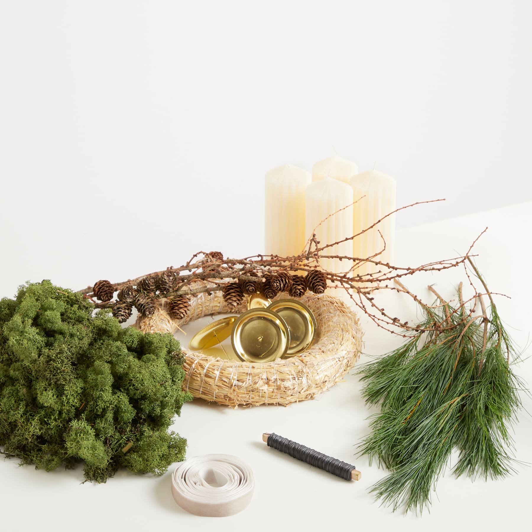 Ein rustikaler Kranz aus Naturmaterialien wie Tannenzweigen, Moos und Tannenzapfen liegt auf einer Holzoberfläche, begleitet von einer Kerze und anderen Dekorationselementen.
