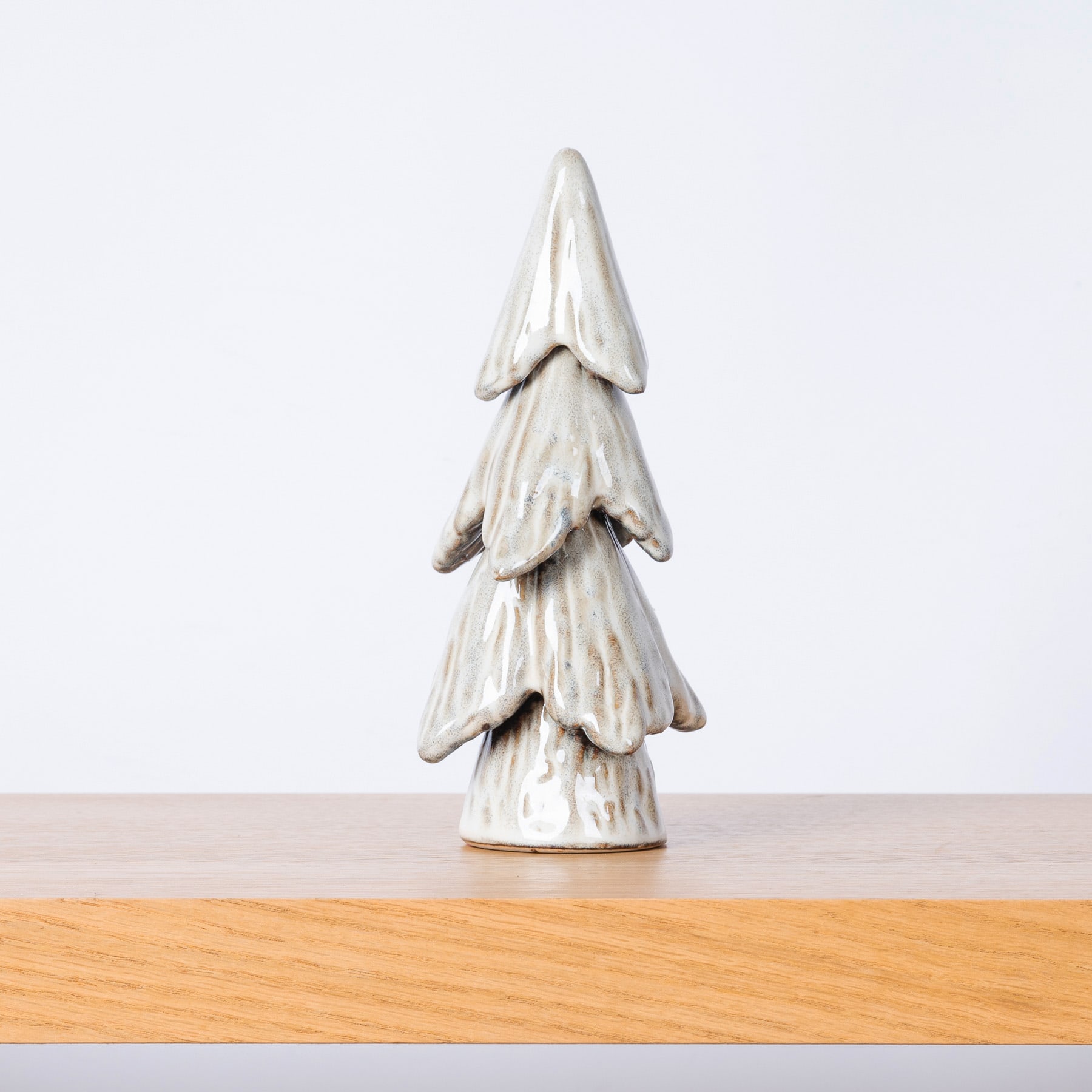 Ein weißes, weihnachtsbaumförmiges Keramikornament steht auf einer Holzoberfläche vor einem schlichten Hintergrund.
