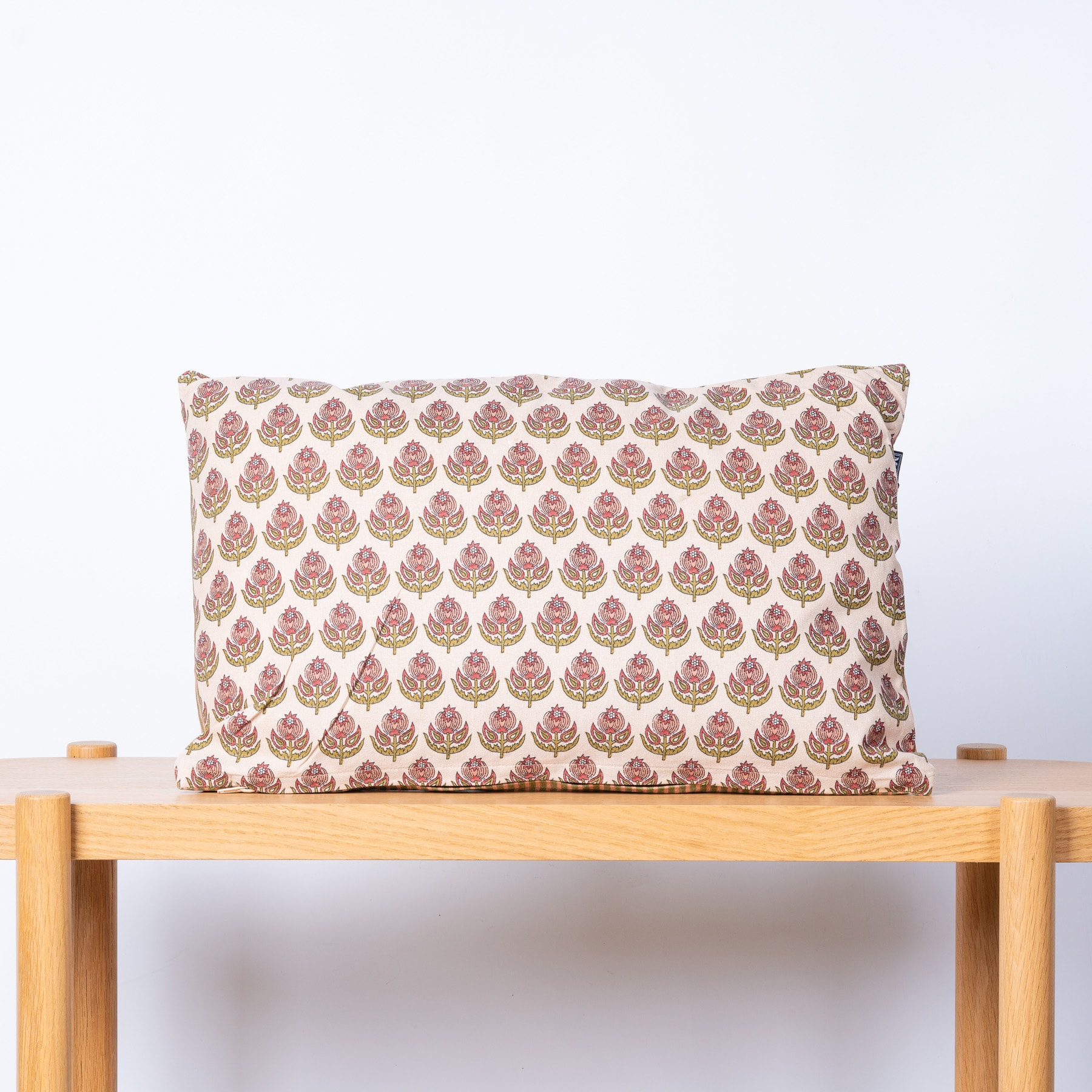 Ein dekorativ gemustertes Kissen liegt auf einer Holzbank vor einem schlichten weißen Hintergrund.