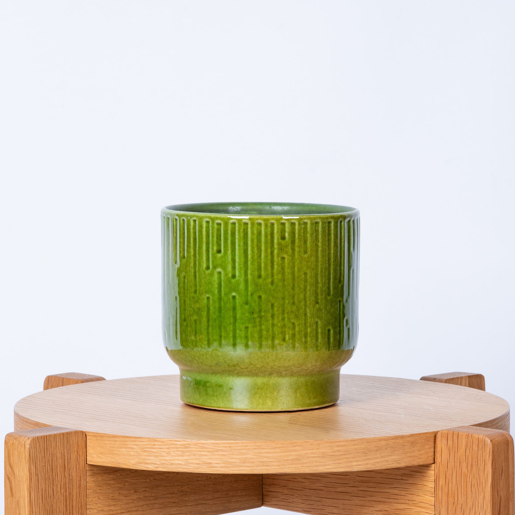 Ein grüner Blumentopf oder Topf aus Keramik steht auf einem Holzständer oder einer Plattform vor einem schlichten weißen Hintergrund.