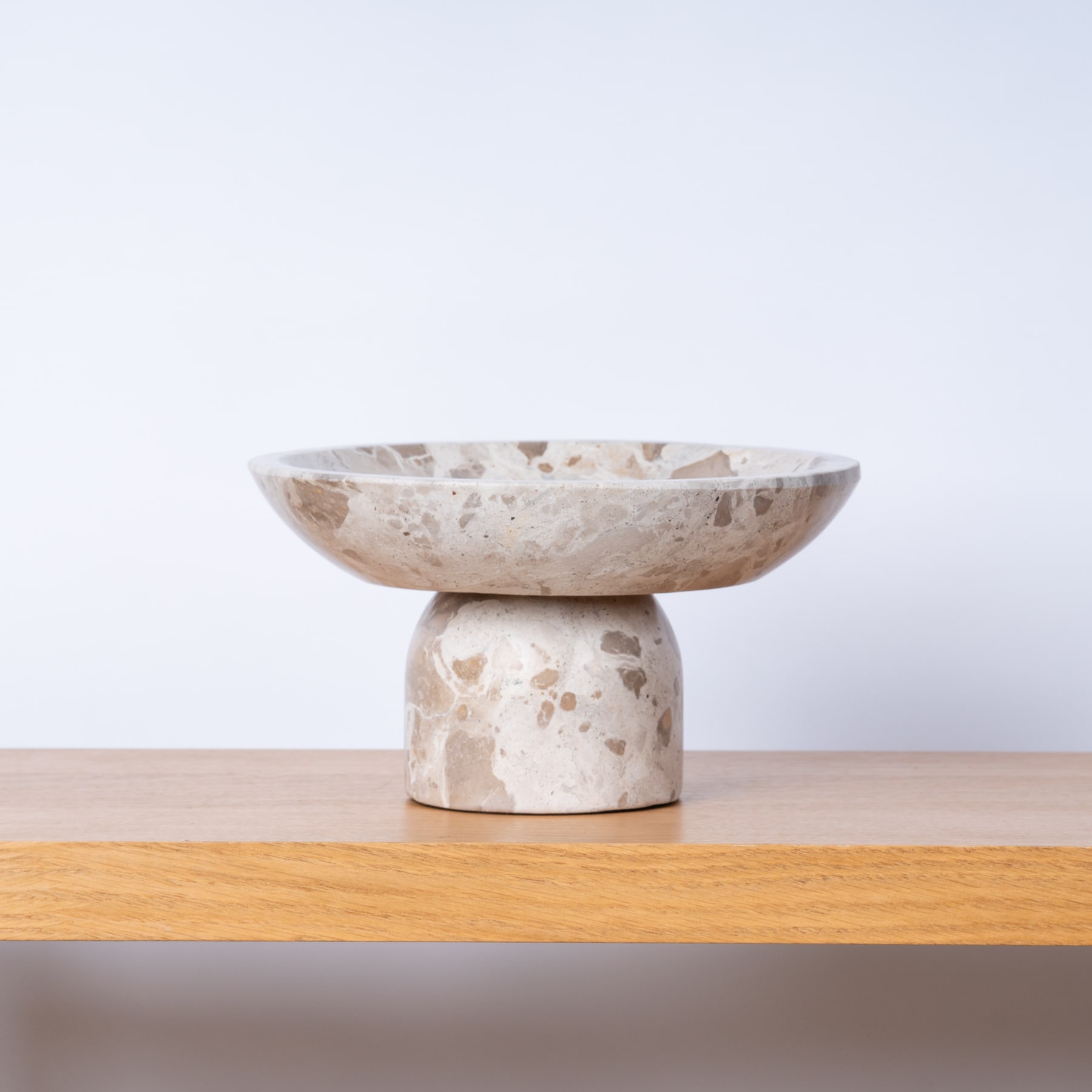 Eine beige Schale im Terrazzo-Stil ruht auf einem Holzsockel vor einem schlichten, hellen Hintergrund.