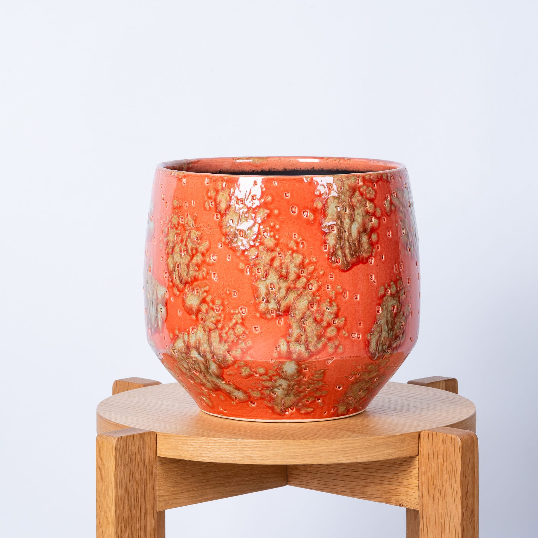 Eine farbenfrohe, strukturierte Keramikschale steht auf einem Holzständer vor einem schlichten weißen Hintergrund.