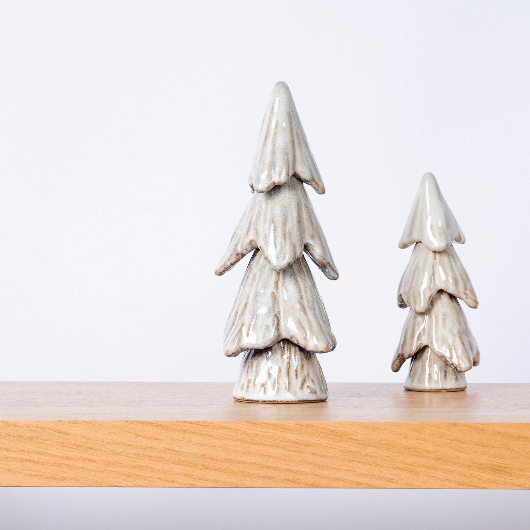 Zwei Keramik-Weihnachtsbäume in unterschiedlichen Größen stehen auf einer Holzoberfläche vor einem schlichten Hintergrund.