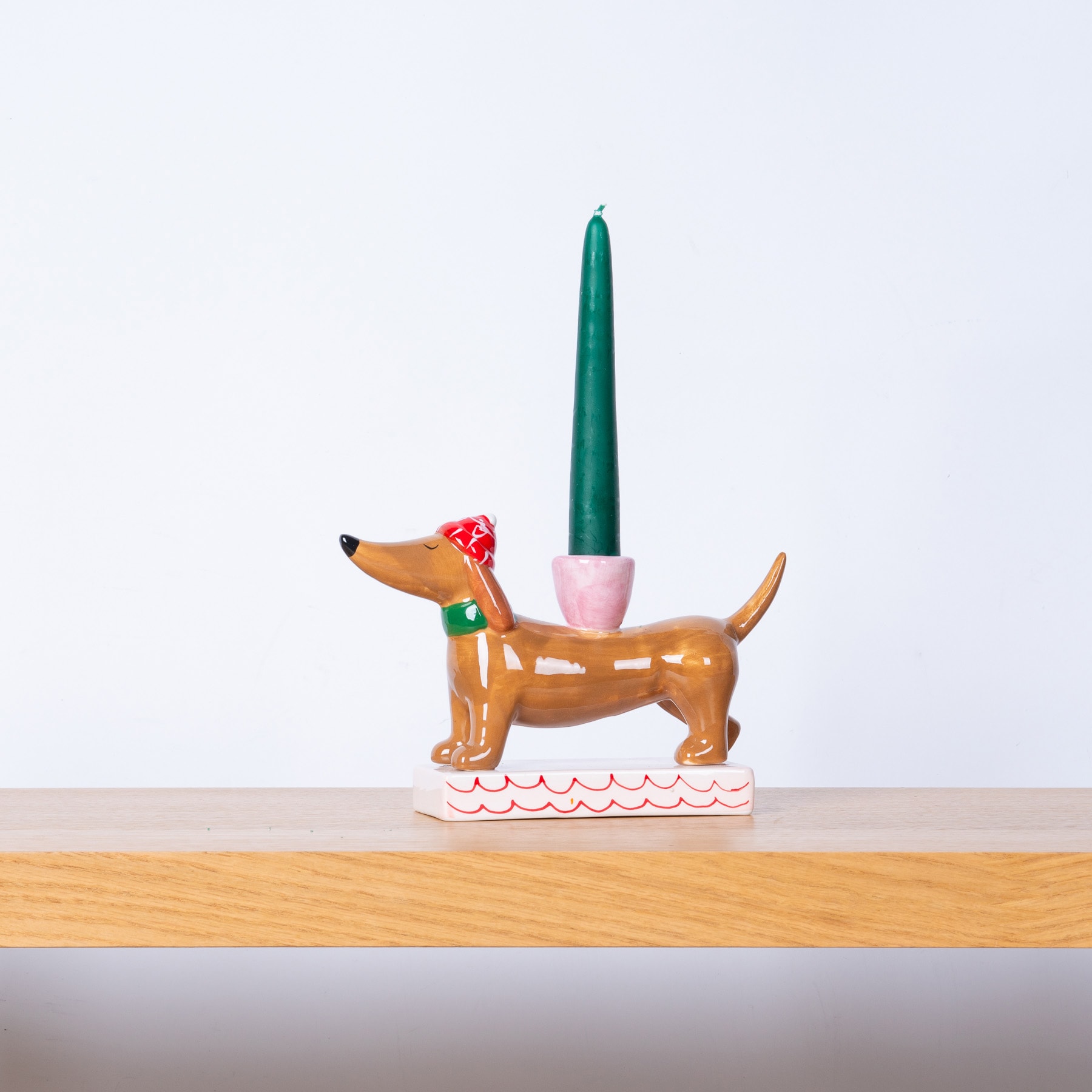 Auf einer Holzfläche steht eine bunte aufblasbare Dackelfigur, auf deren Rücken eine grüne Kerze steht.