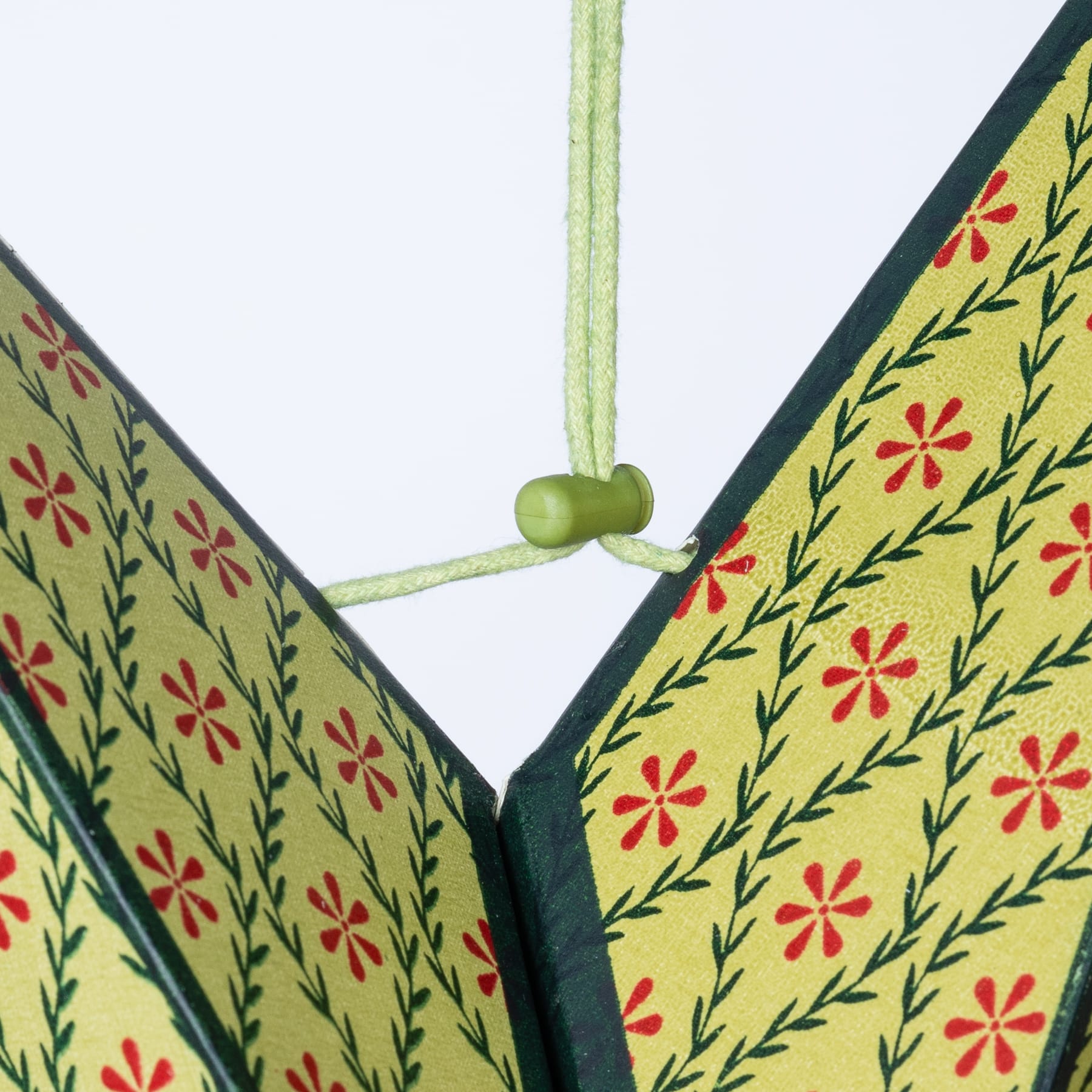 Das Bild zeigt einen bunten, gemusterten Stoff mit Blumenmustern in Grün-, Gelb- und Rottönen und einer in der Mitte zu einem Knoten gebundenen grünen Kordel oder Schnur.