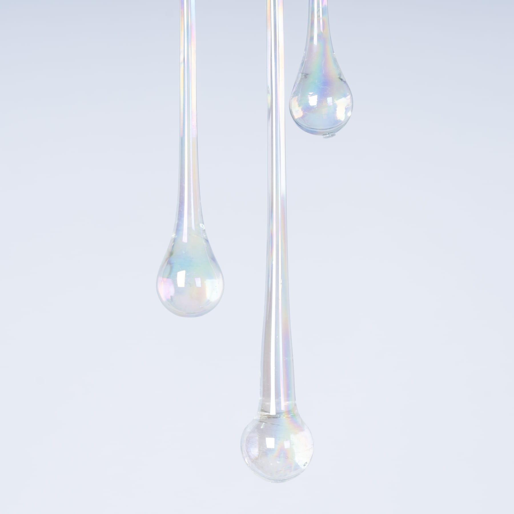 Zarte Glastropfen, die jeweils ein prismatisches Spektrum reflektieren, hängen vor einem hellblauen Hintergrund.