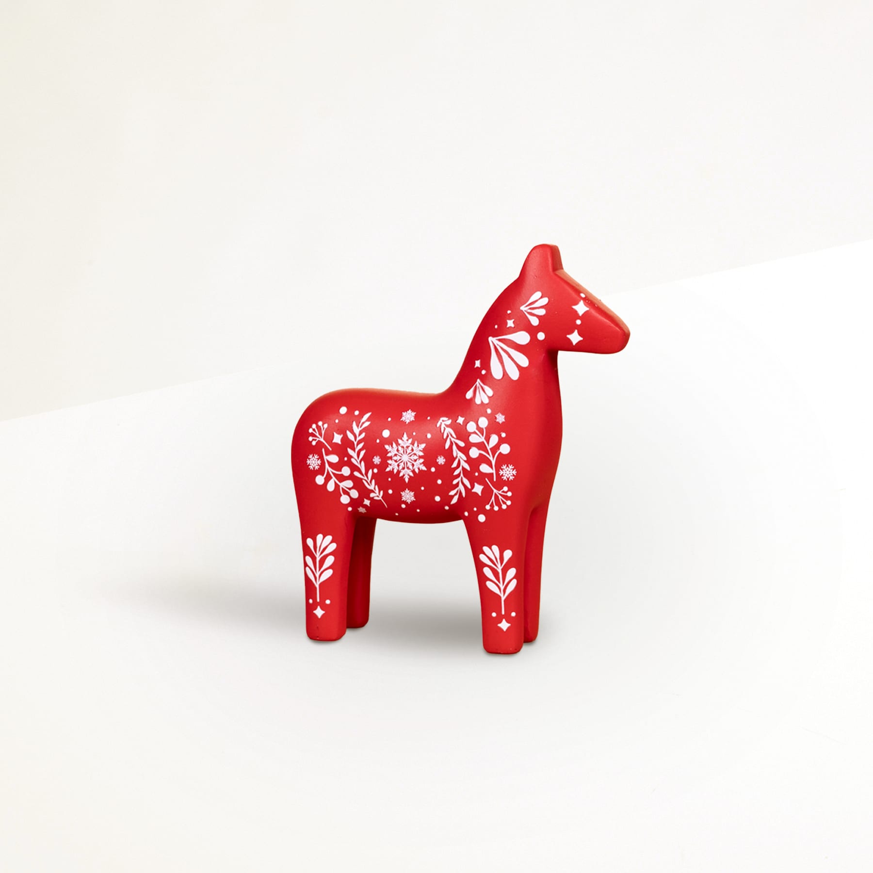 Eine rote Pferdefigur aus Holz mit komplizierten weißen Blumenmustern steht vor einem schlichten weißen Hintergrund.