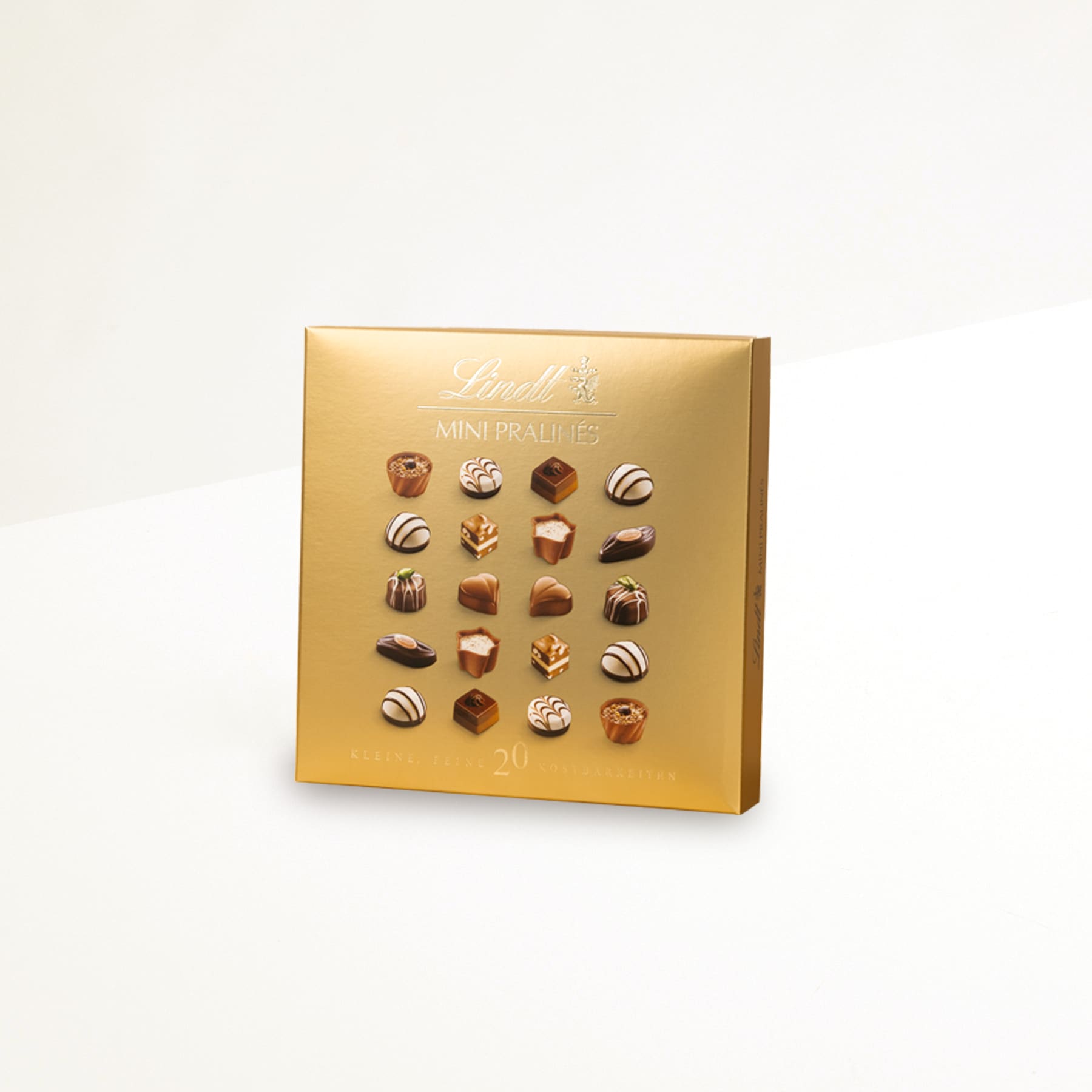 Vor einem schlichten weißen Hintergrund wird eine goldfarbene Schachtel mit einer Auswahl verschiedener Schokoladenbonbons oder Trüffel präsentiert.