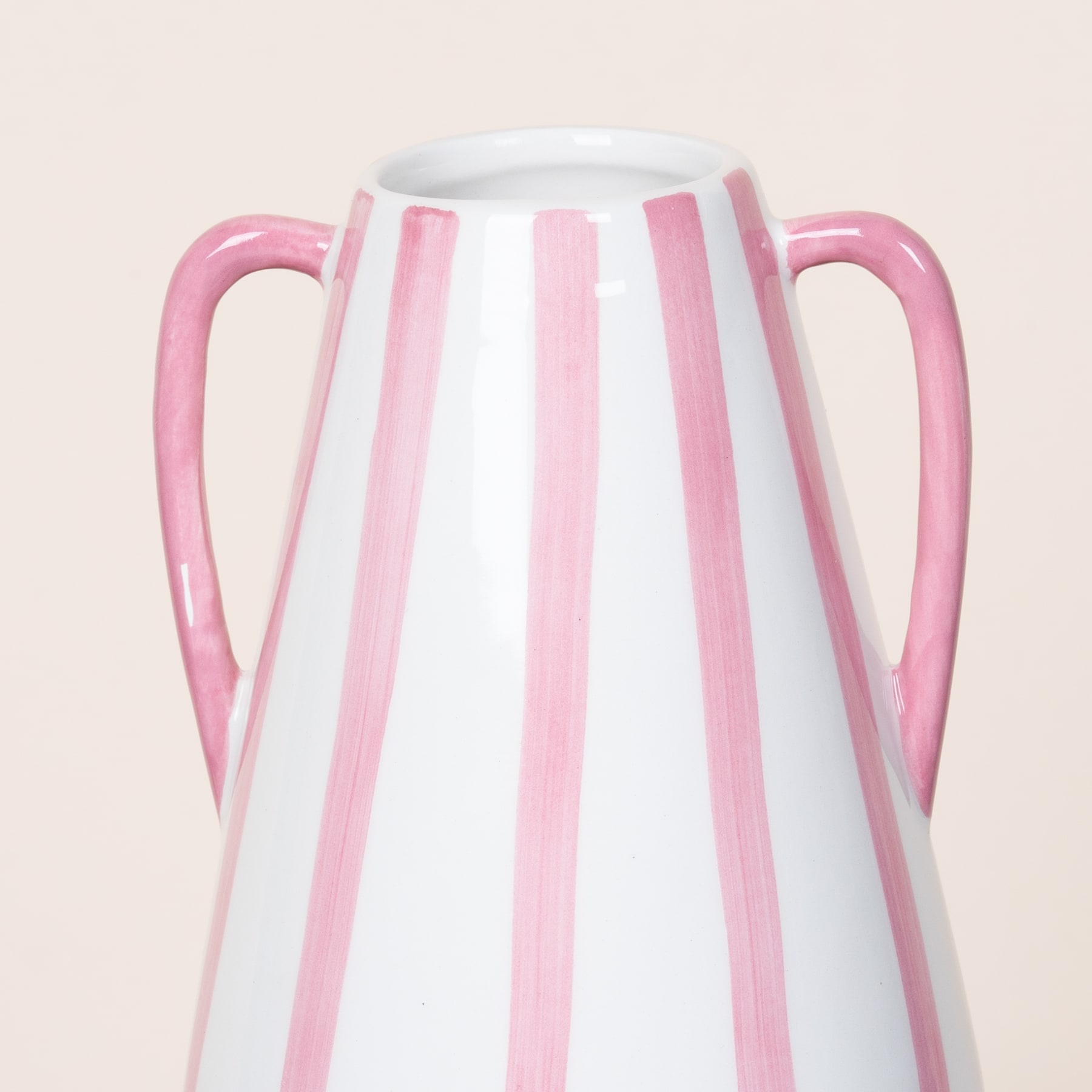 Eine weiße Keramikvase mit vertikalen rosa Streifen vor einem schlichten beigen Hintergrund.