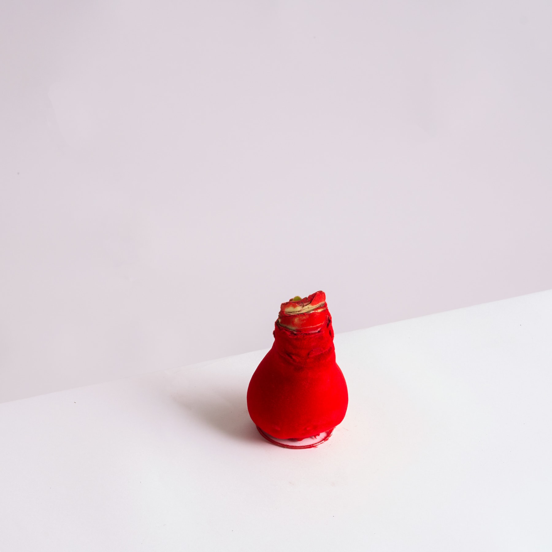 Eine leuchtend rote Glasvase oder -flasche steht auf einer schlichten weißen Oberfläche vor einem hellen Hintergrund.