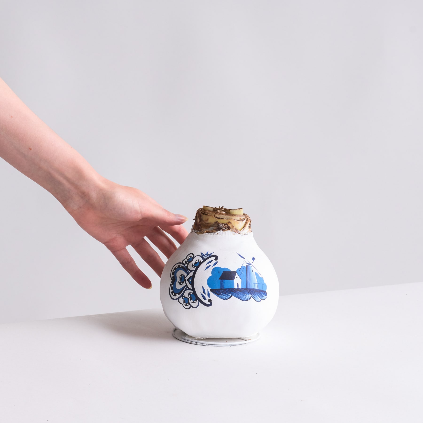 Eine Hand hält sanft ein Keramikgefäß oder eine Vase mit einem dekorativen blau-weißen Muster vor einem schlichten weißen Hintergrund.