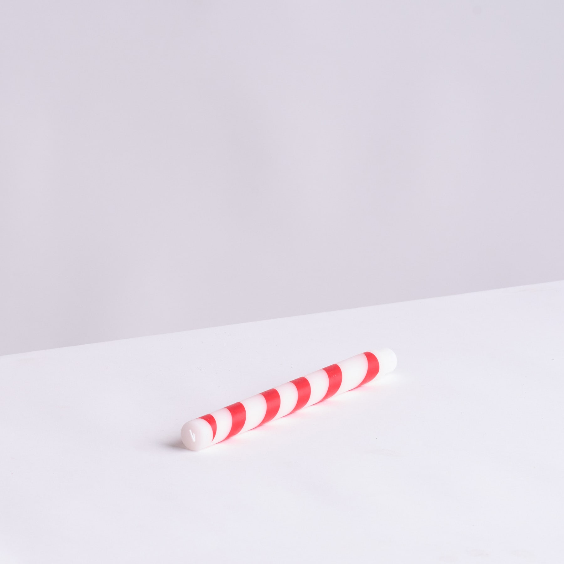 Ein weiß-rot gestreiftes, zuckerstangenähnliches Objekt liegt auf einem schlichten weißen Hintergrund.