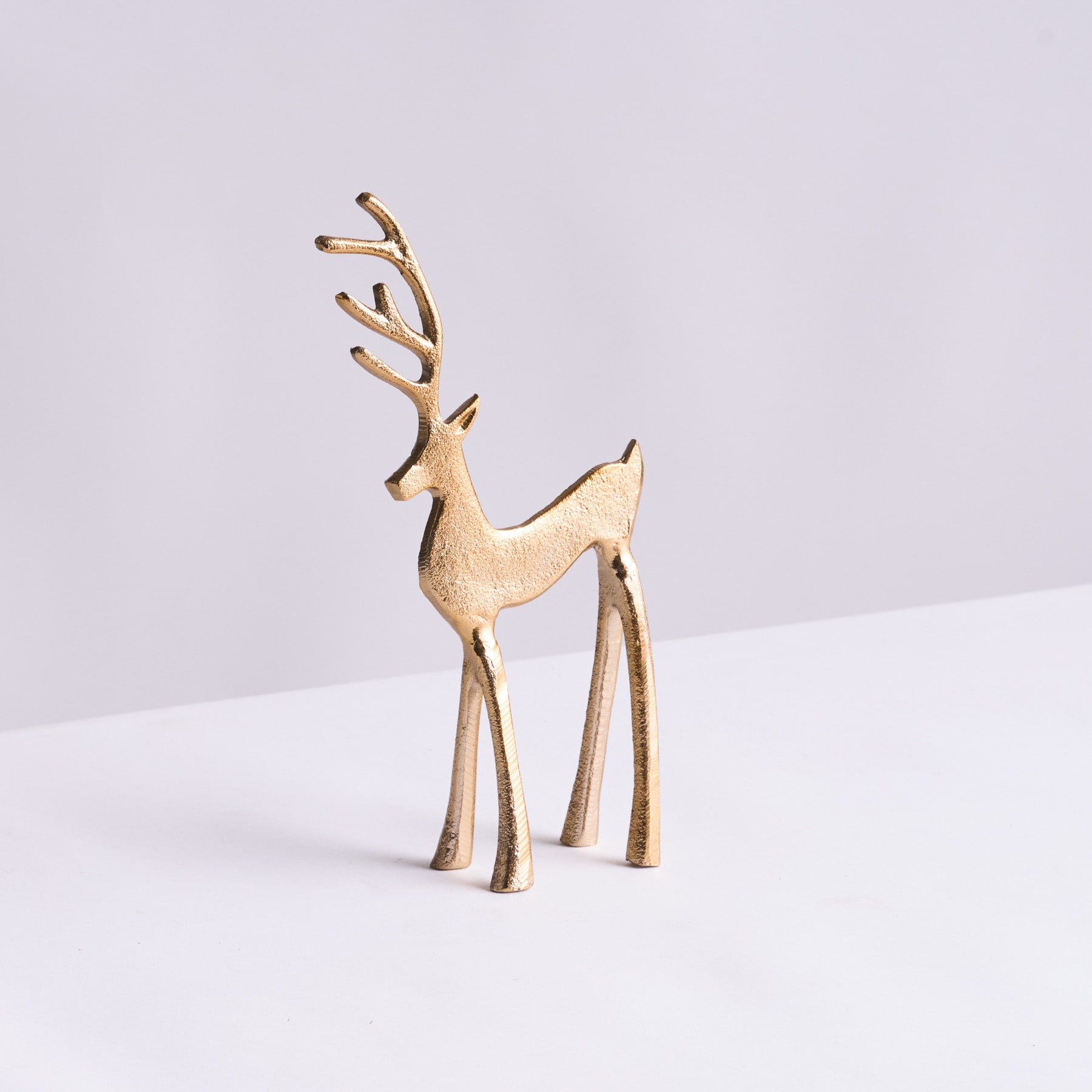 Auf einem schlichten weißen Hintergrund steht eine hölzerne Hirschfigur, deren schlanke Beine und Geweih ein minimalistisches, elegantes Design ergeben.