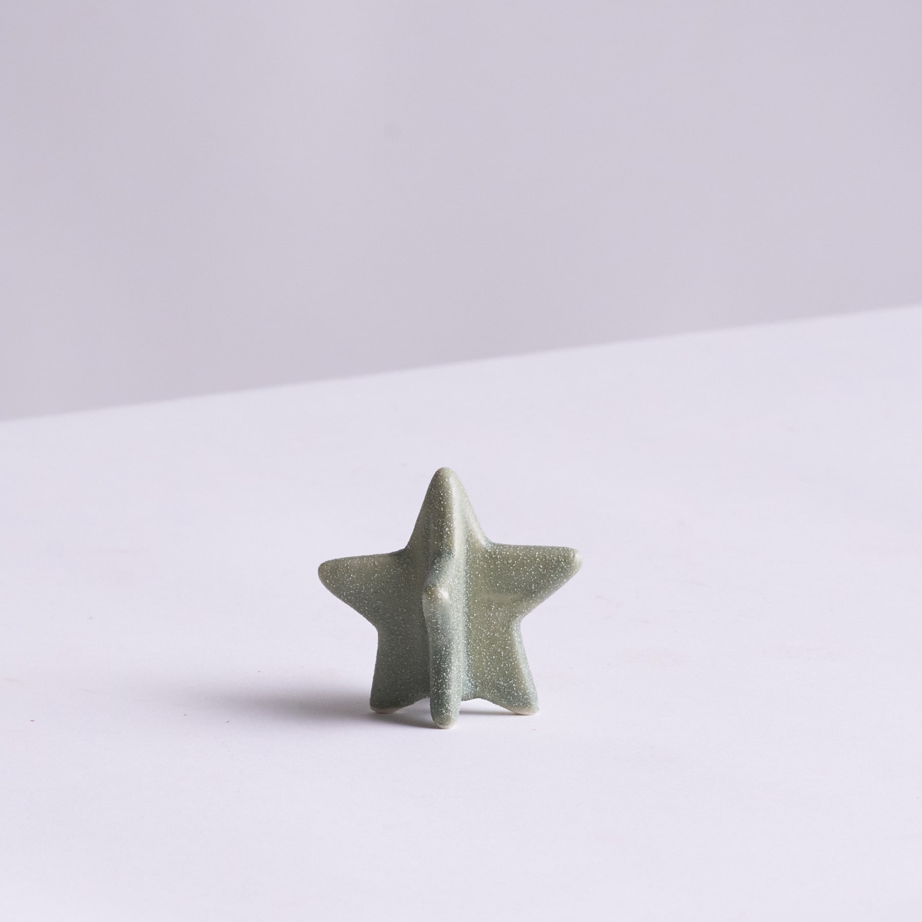 Ein einfaches, minimalistisches Bild mit einem kleinen, grauen, sternförmigen Objekt vor einem schlichten, hellen Hintergrund.