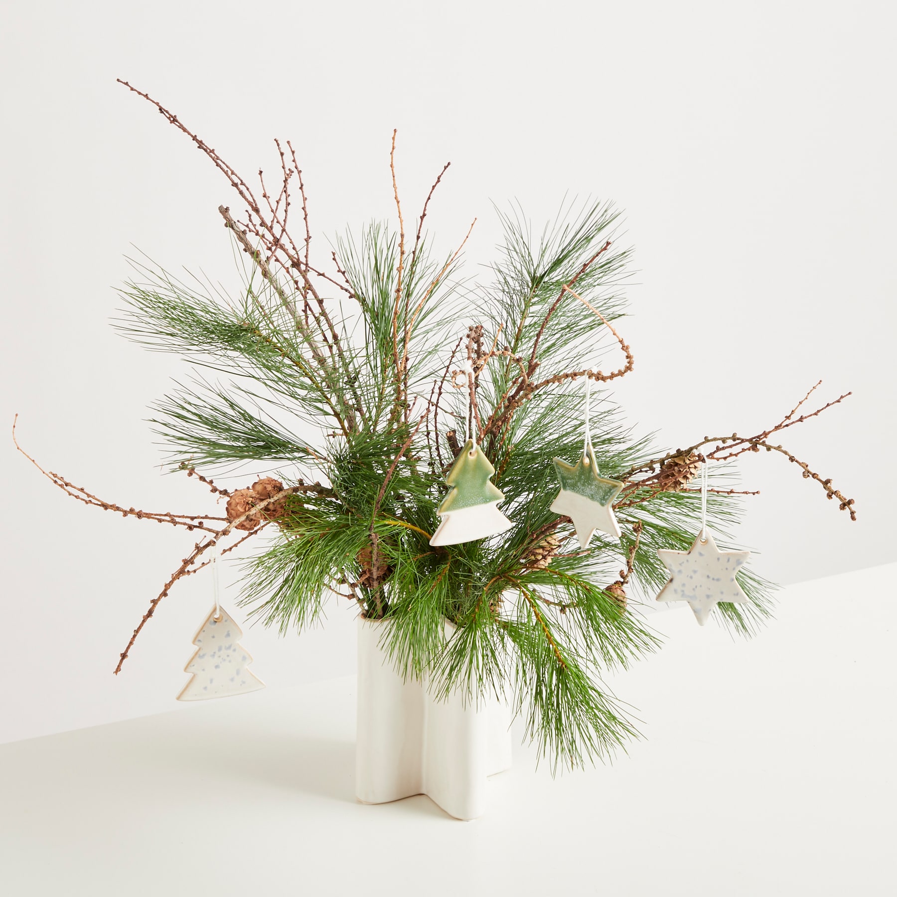 Auf einer schlichten weißen Oberfläche steht eine Vase mit einem farbenfrohen Arrangement aus Tannenzweigen, Beeren und weißen Blumen.