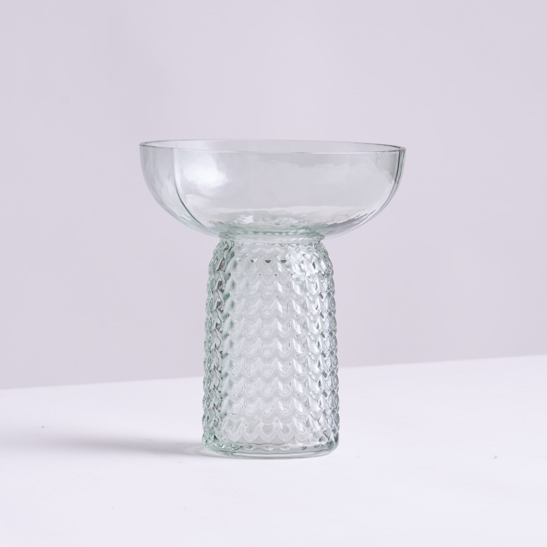 Eine klare Glasschale ruht auf einem strukturierten Glassockel vor einem schlichten weißen Hintergrund.