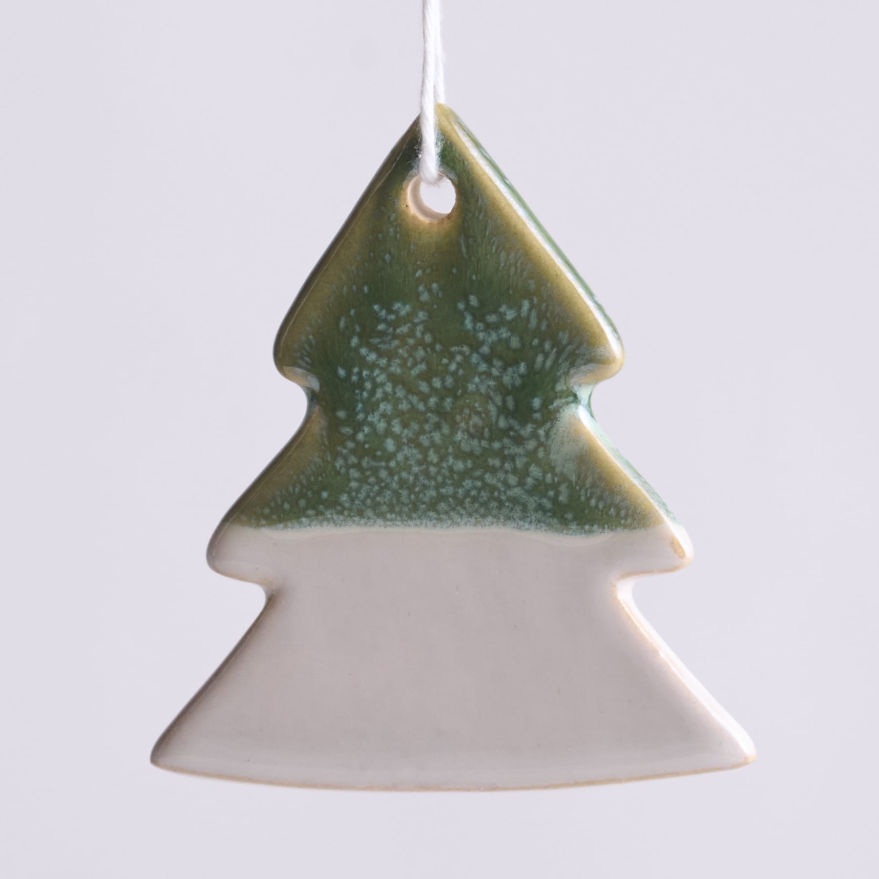 Ein Christbaumschmuck aus Keramik in Form einer Kiefer, mit grün-weiß glasierter Oberfläche und einer Aufhängeöse an der Spitze.