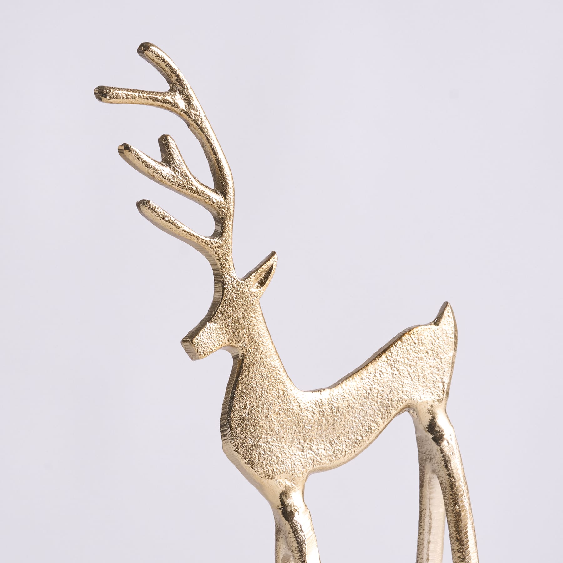 Vor einem schlichten weißen Hintergrund steht eine goldfarbene Hirschfigur mit kunstvollem Geweih.
