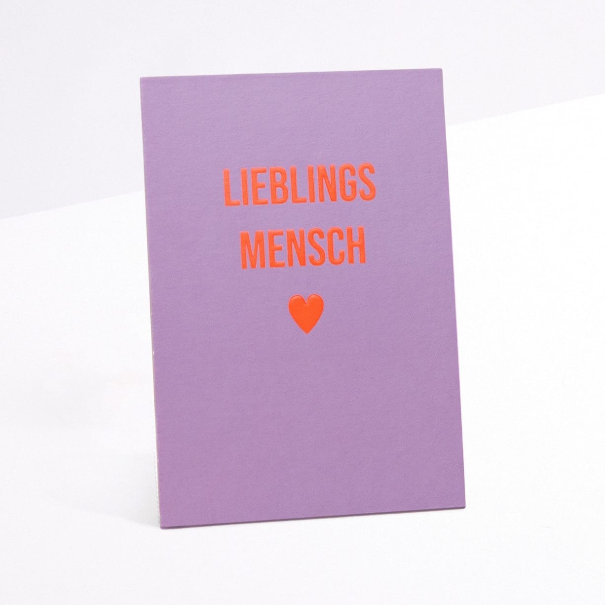 Eine violette Karte mit dem deutschen Text „LIEBLINGS MENSCH“ in roten Buchstaben und einem kleinen roten Herzsymbol unter dem Text.