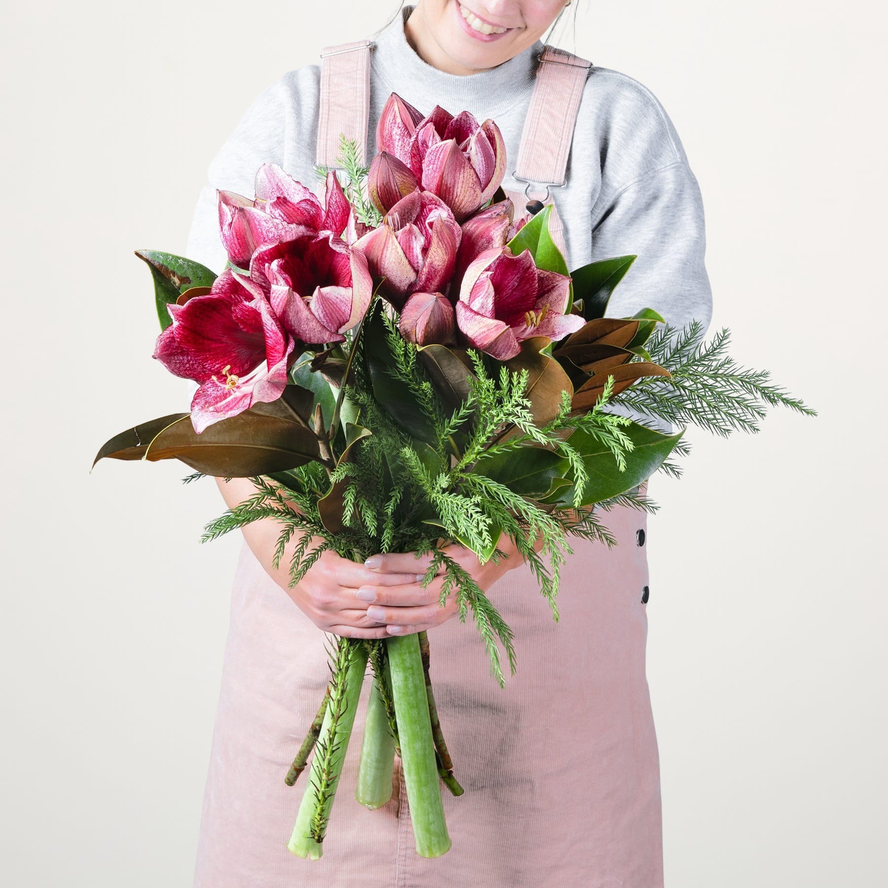 Eine Person in einem hellen Pullover hält einen Strauß leuchtend rosa Tulpen vor einem schlichten weißen Hintergrund.