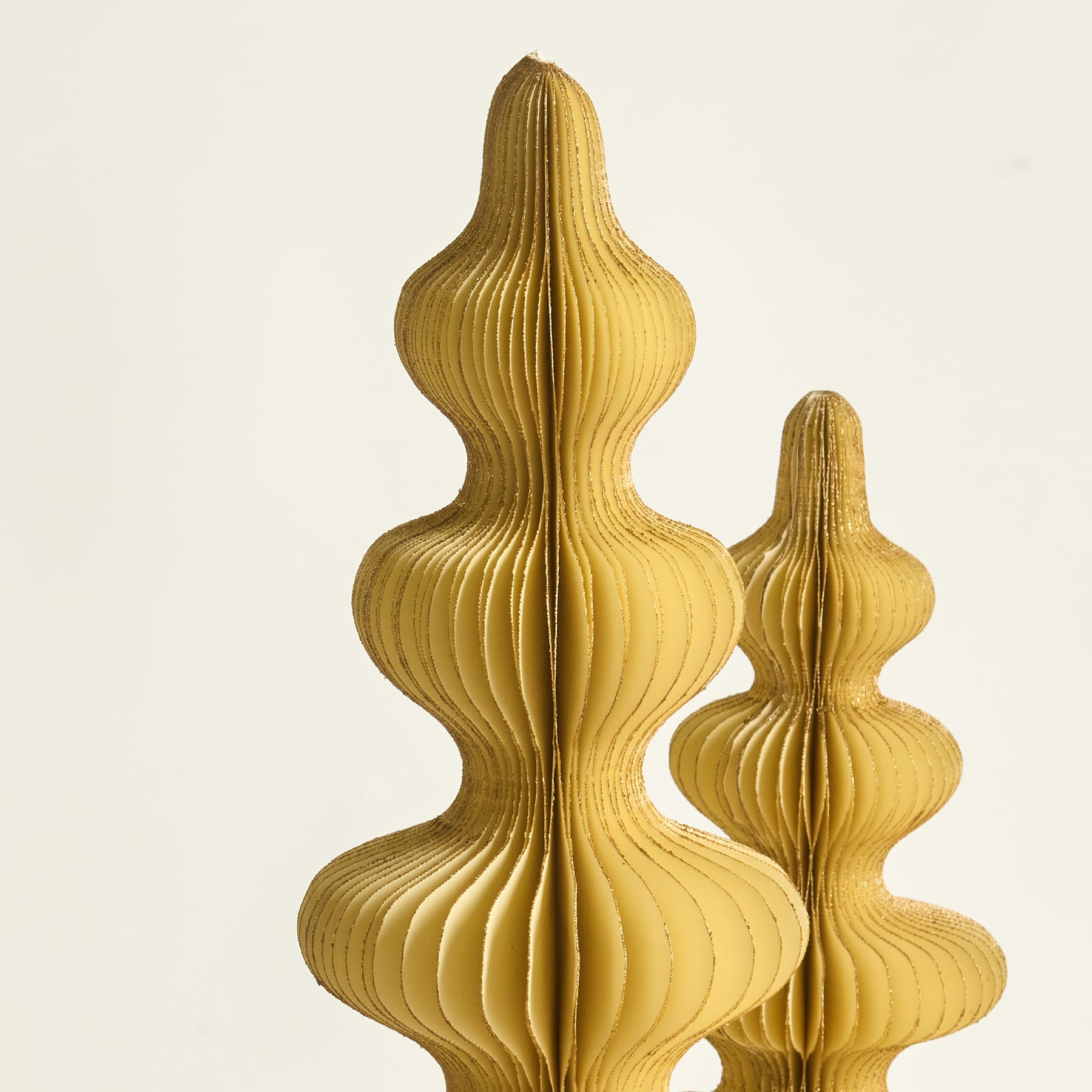 Zwei kunstvolle, goldfarbene Papierskulpturen mit wellenförmigen Formen stehen vor einem schlichten, cremefarbenen Hintergrund.