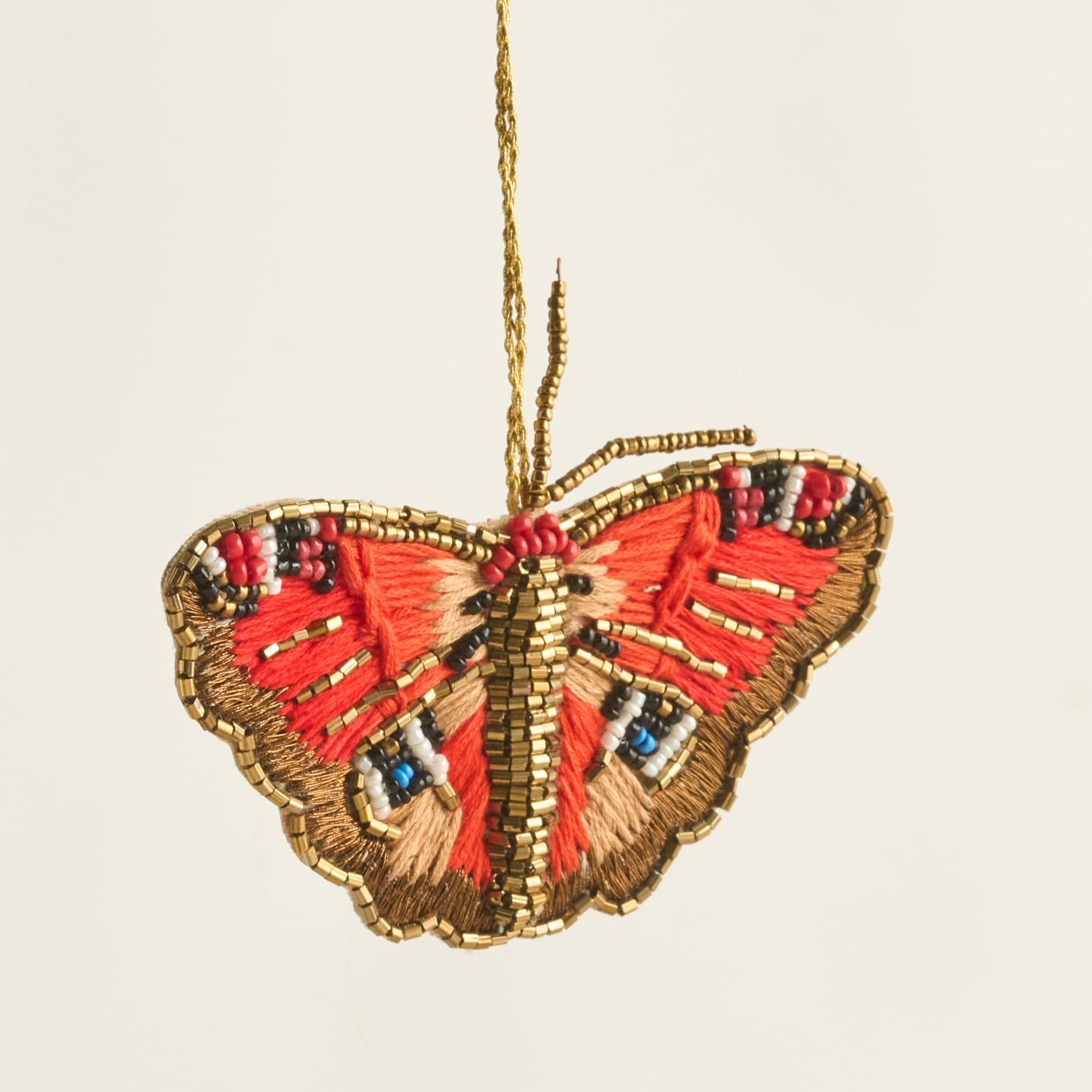 Ein lebendiges, aufwendig gesticktes Schmetterlingsornament in Rot-, Gold- und Blautönen auf neutralem Hintergrund.