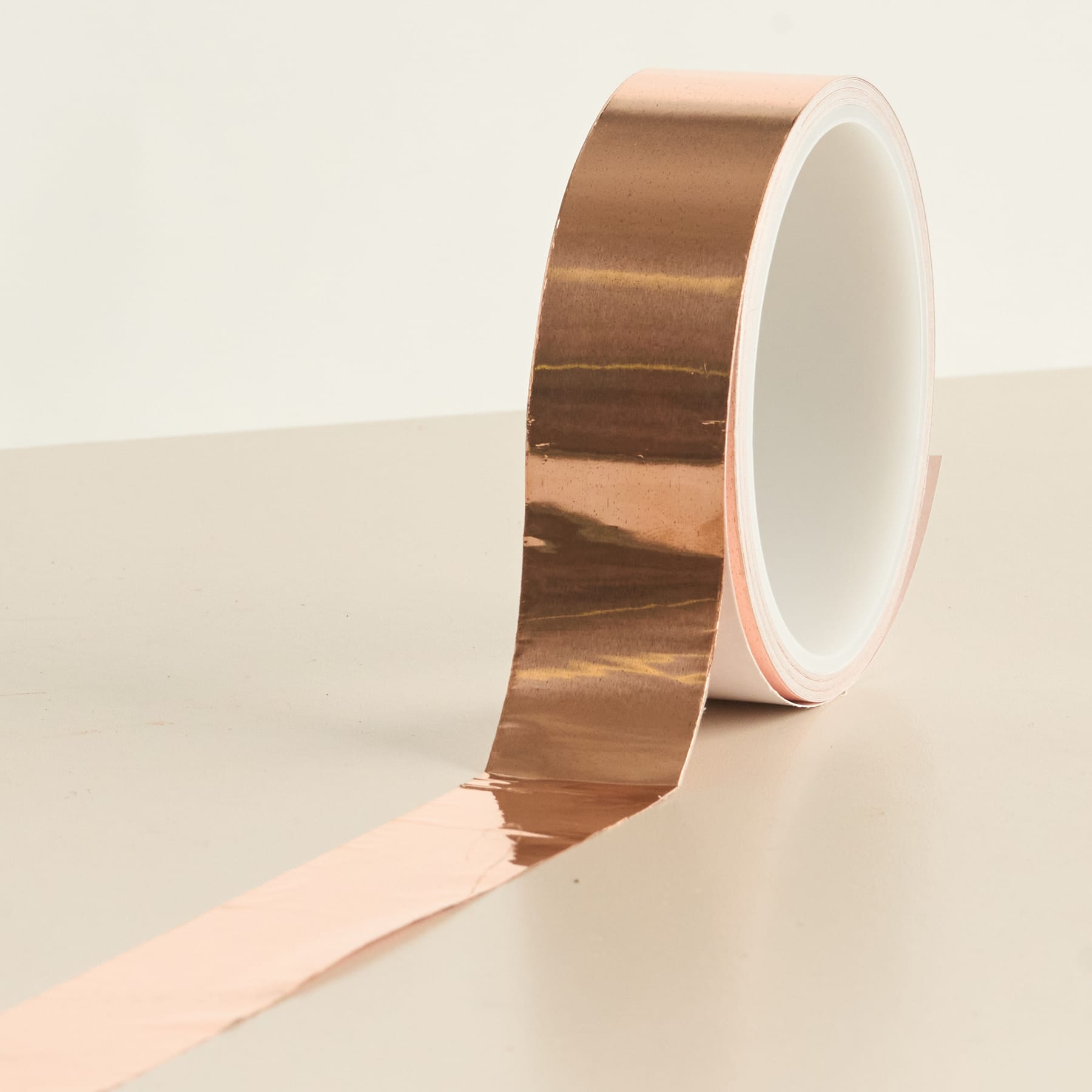 Eine Rolle glänzendes kupferfarbenes Klebeband liegt auf einer schlichten, hellen Oberfläche.