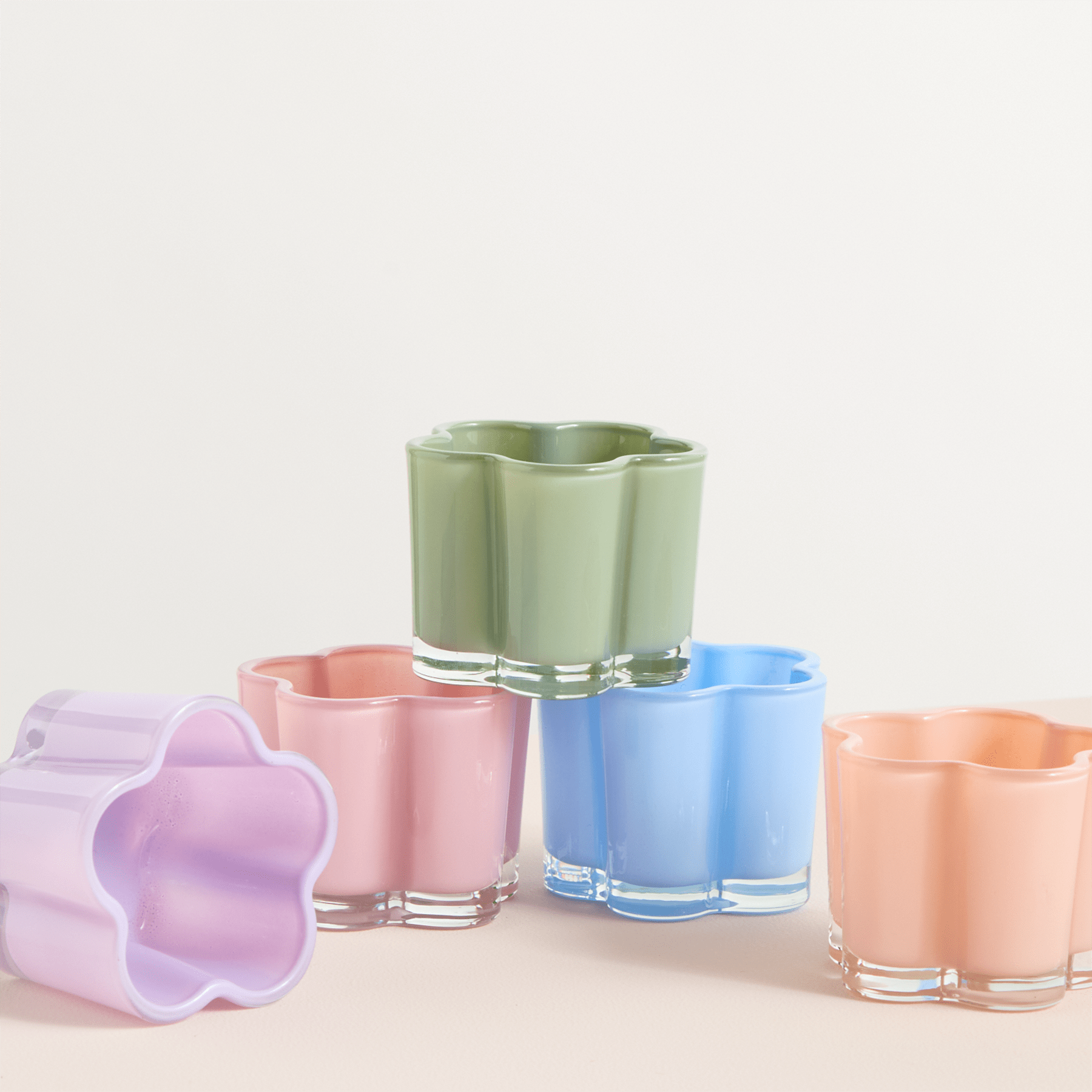 Eine Sammlung farbenfroher, pastellfarbener Glasbecher oder Vasen, die auf einem schlichten Hintergrund angeordnet sind.