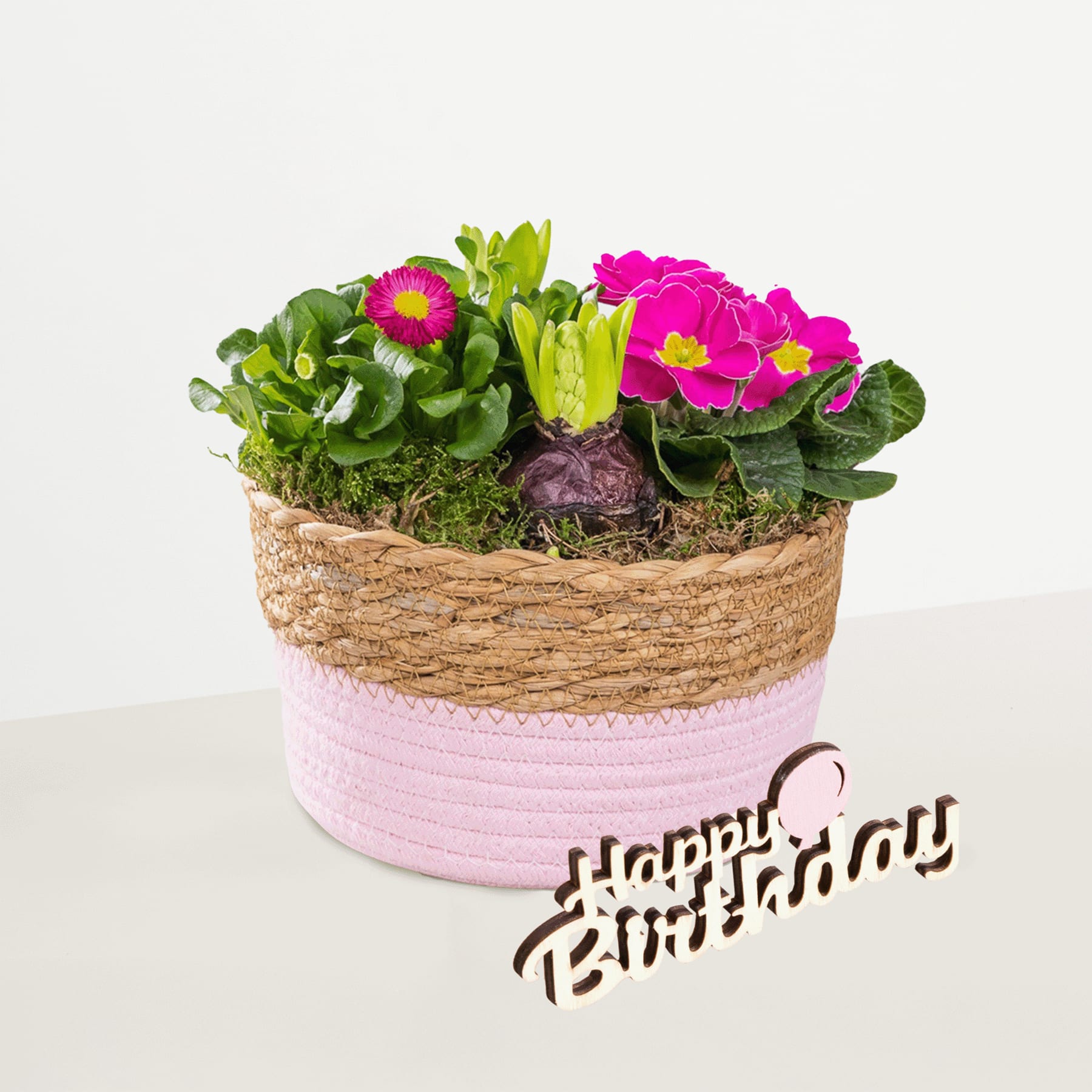 Ein farbenfrohes Arrangement aus leuchtend rosa und grünen Blumen in einem geflochtenen Korb, begleitet von einer „Happy Birthday“-Nachricht.