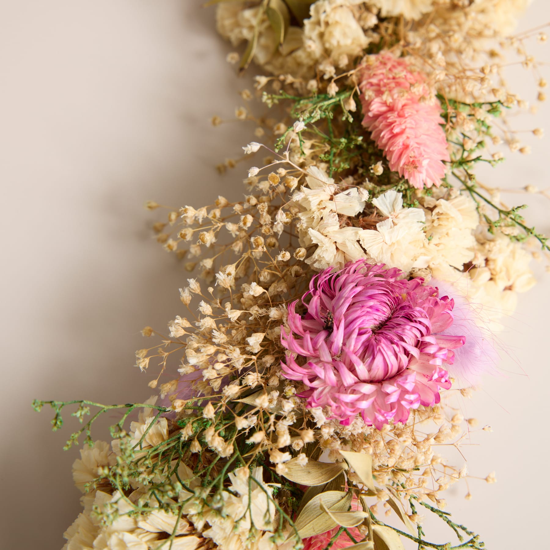 Ein lebendiger Strauß rosa und weißer Blumen, darunter eine große Dahlie, eingebettet zwischen zartem Grün und getrockneten Blumenelementen, vor einem weichen, neutralen Hintergrund.