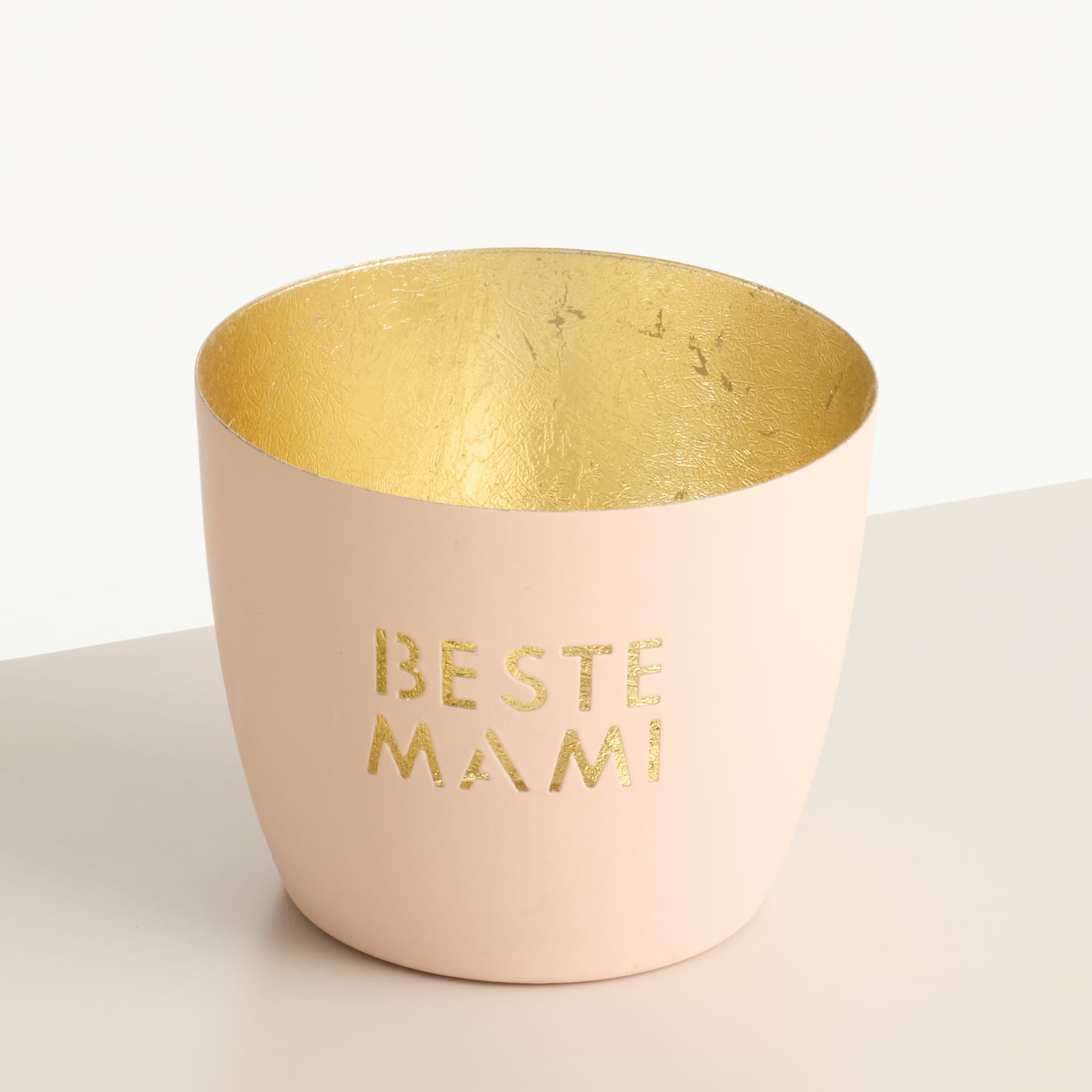 Eine rosa Keramiktasse mit dem in Gold geschriebenen Text „BESTE MAMI“ (Beste Mama) auf der Oberfläche, auf einem schlichten weißen Hintergrund.