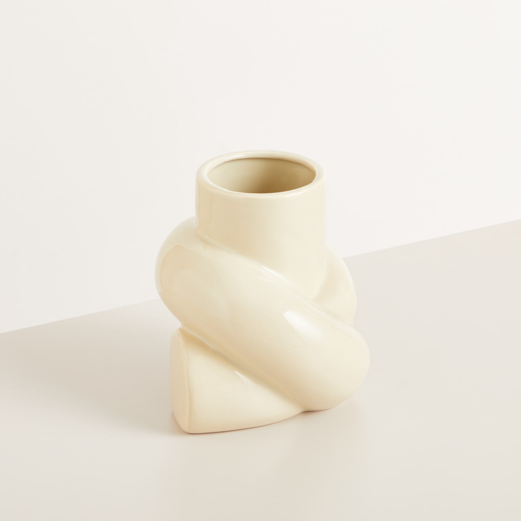 Eine einfache, minimalistische Keramikvase mit einer gedrehten, skulpturalen Form steht auf einer schlichten, hellen Oberfläche.