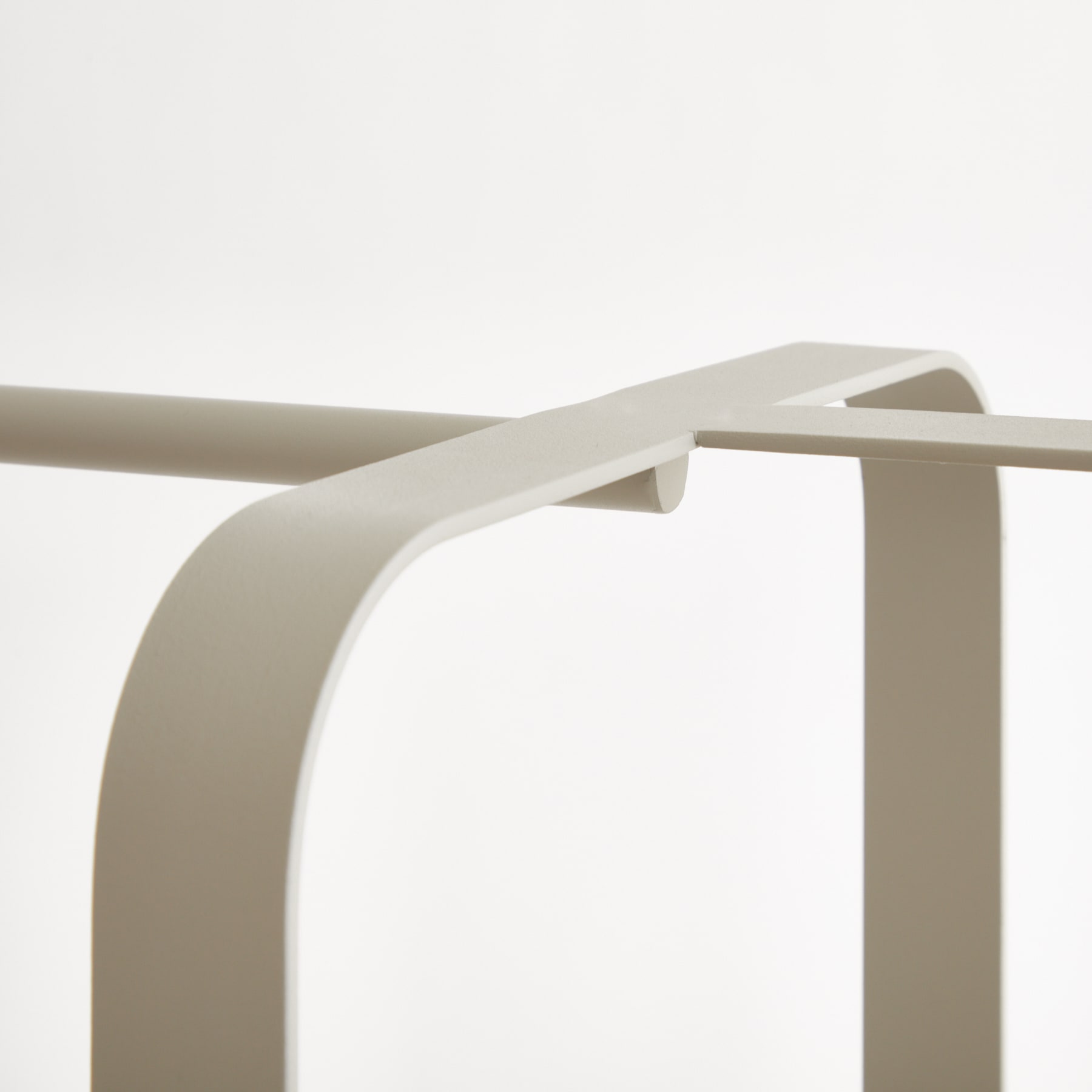 Ein minimalistischer, geschwungener Metallrahmen in einem neutralen Beigeton steht vor einem schlichten weißen Hintergrund.