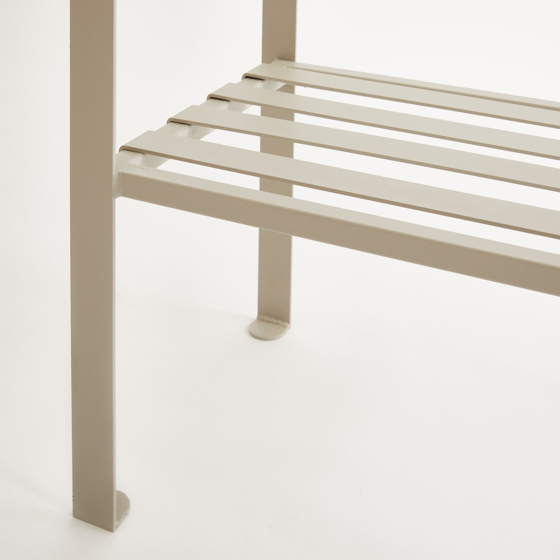 Eine einfache, minimalistische Bank mit horizontalen Latten und einer neutralen Beigefarbe vor einem schlichten weißen Hintergrund.