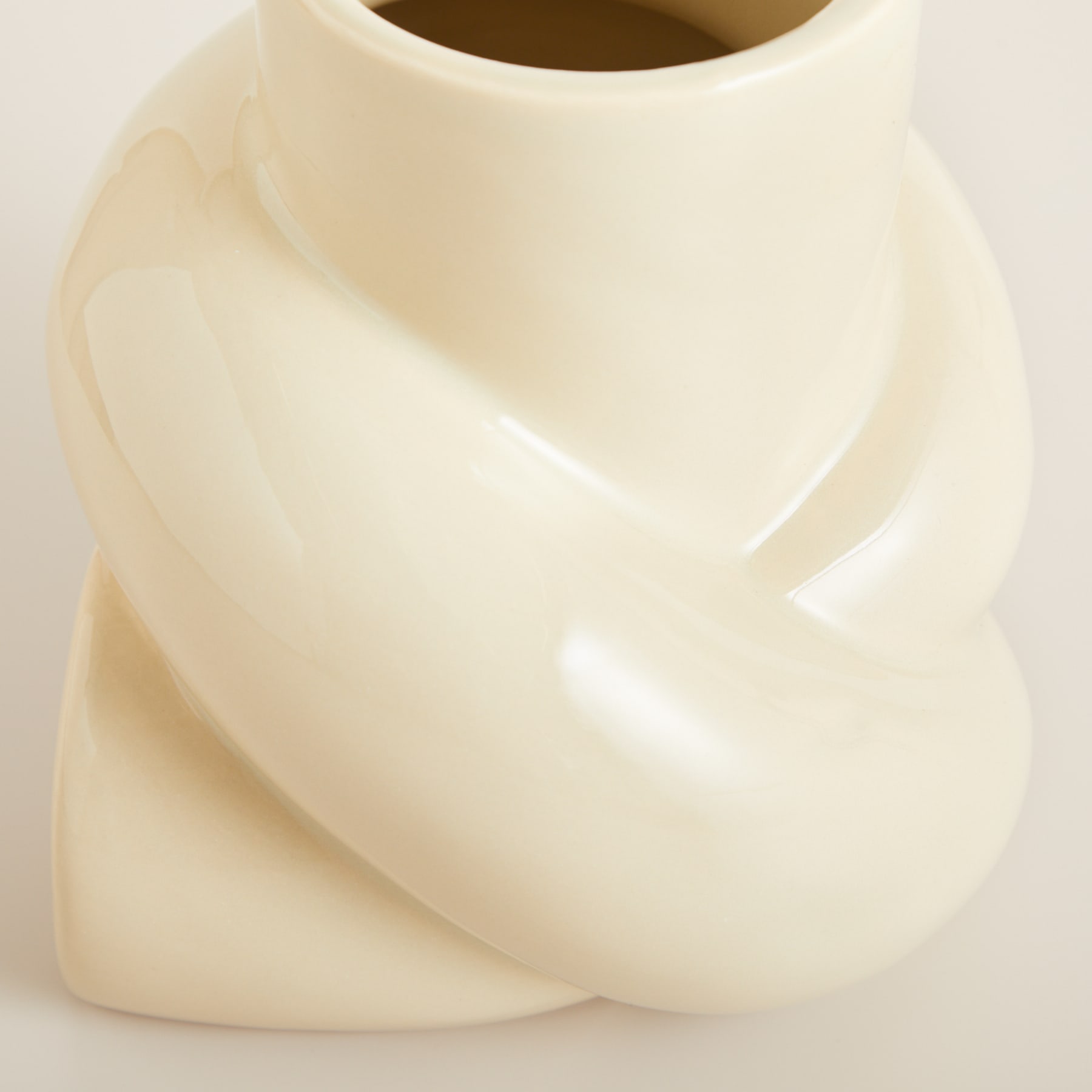 Eine glatte, cremefarbene Keramikvase mit geschwungener, abstrakter Form füllt den Rahmen vor einem schlichten, hellen Hintergrund.