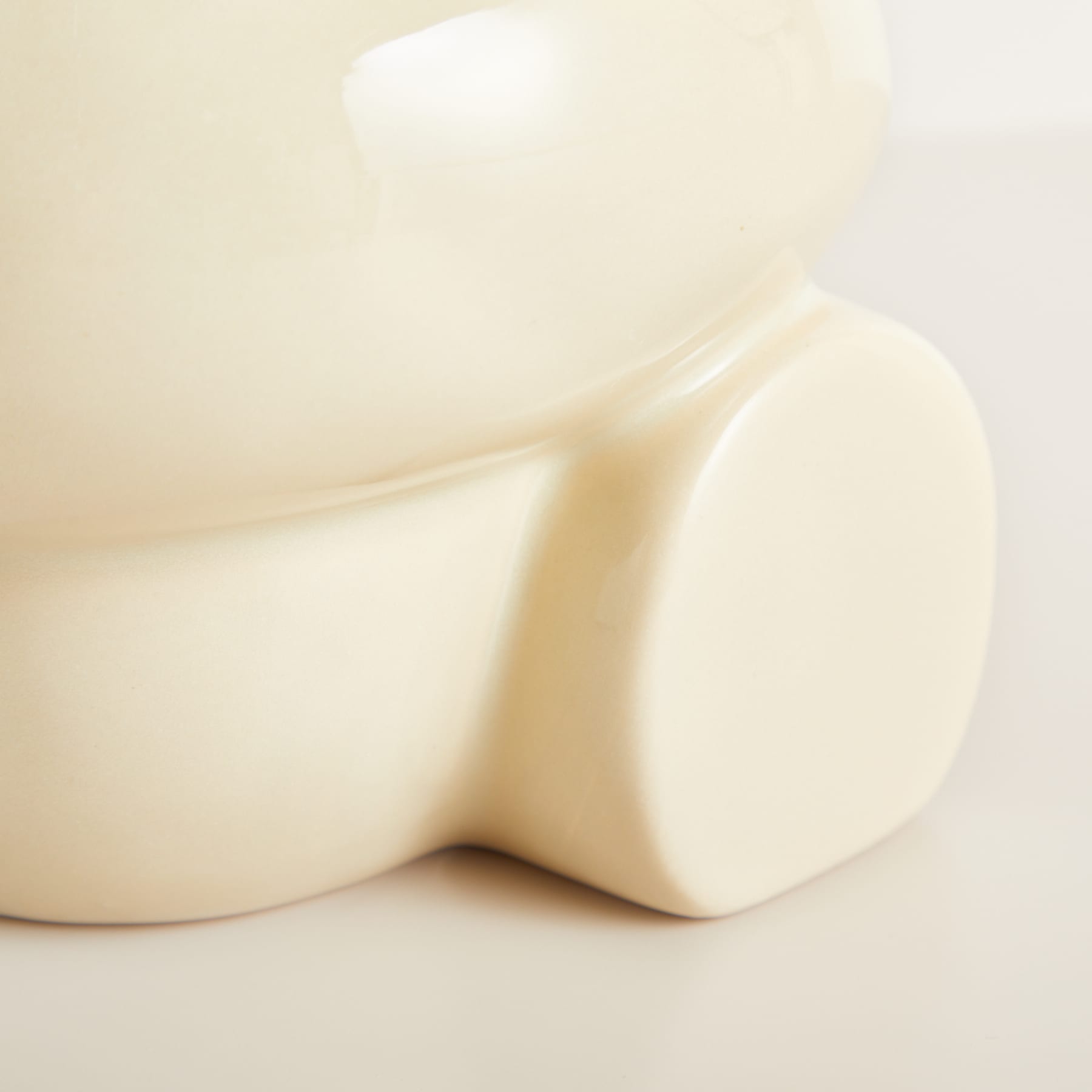 Ein weiches, cremefarbenes Objekt mit einer glatten, geschwungenen Oberfläche füllt den Rahmen und schafft eine minimalistische und abstrakte Komposition.