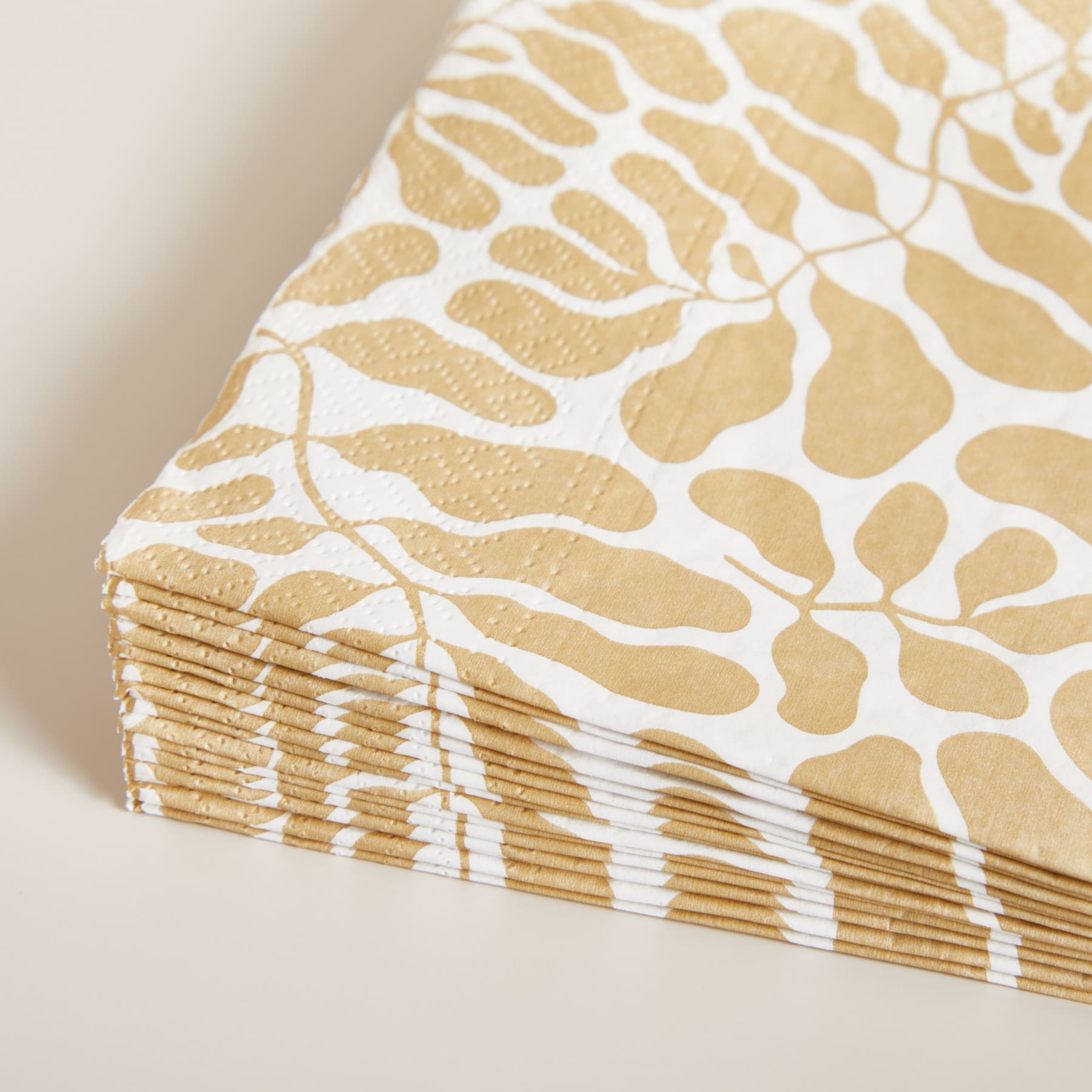 Ein Stapel beige und weiß gemusterter Papierservietten oder Taschentücher mit einem strukturierten, organisch wirkenden Design, das an Tiermuster oder Tarnmuster erinnert.